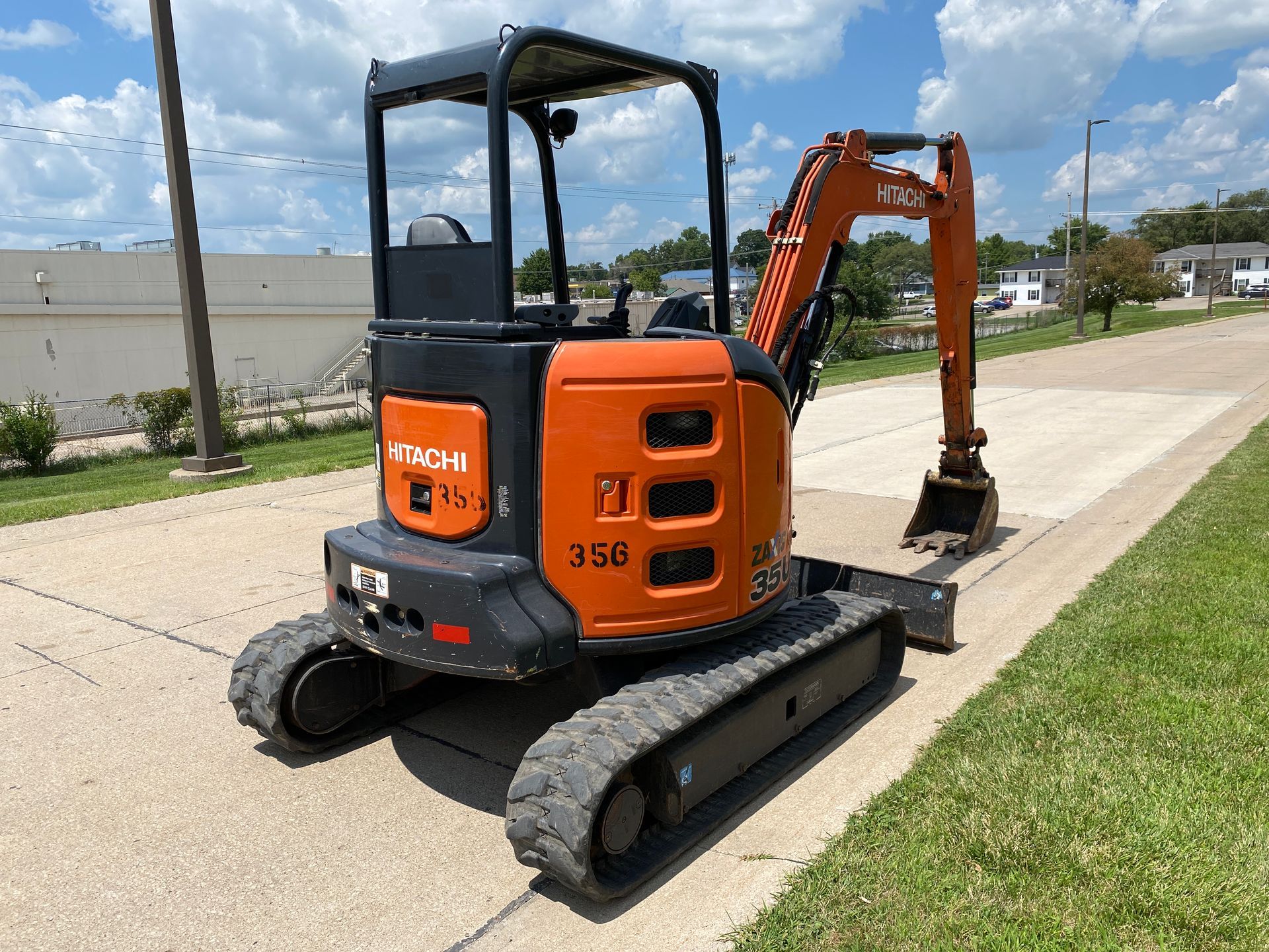 Orange and black Hitachi excavator on concrete, parked outdoors, with cloudy sky background.