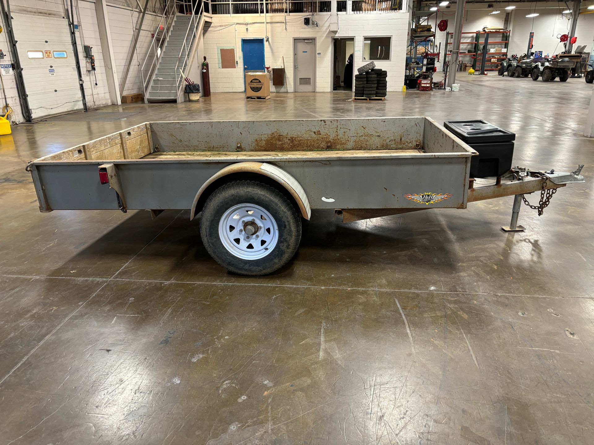 Gray utility trailer with a single wheel, in an industrial setting.