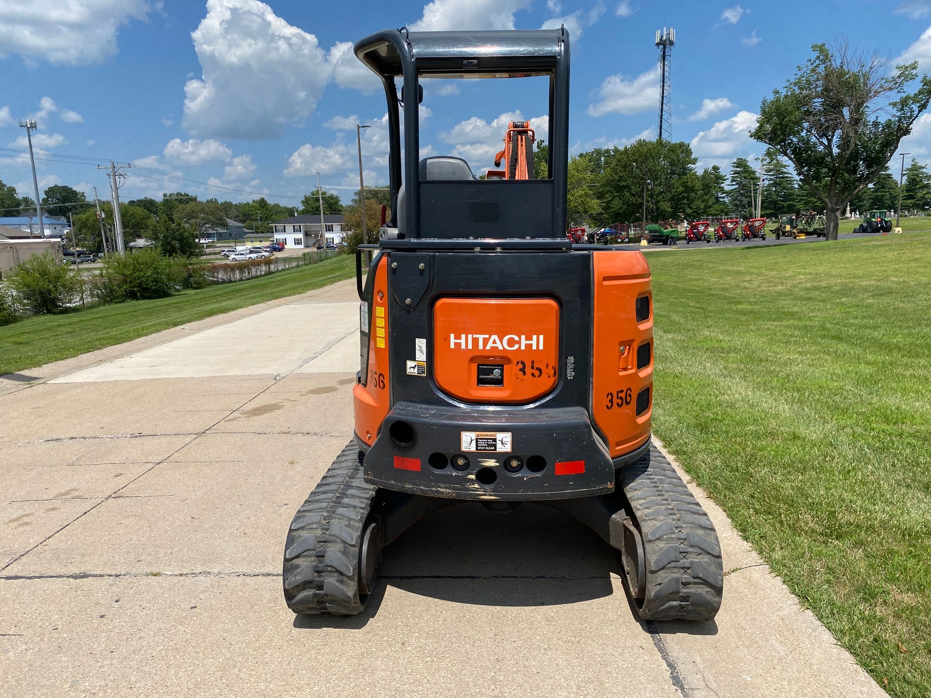 Orange and black Hitachi mini excavator on asphalt, sunny day.