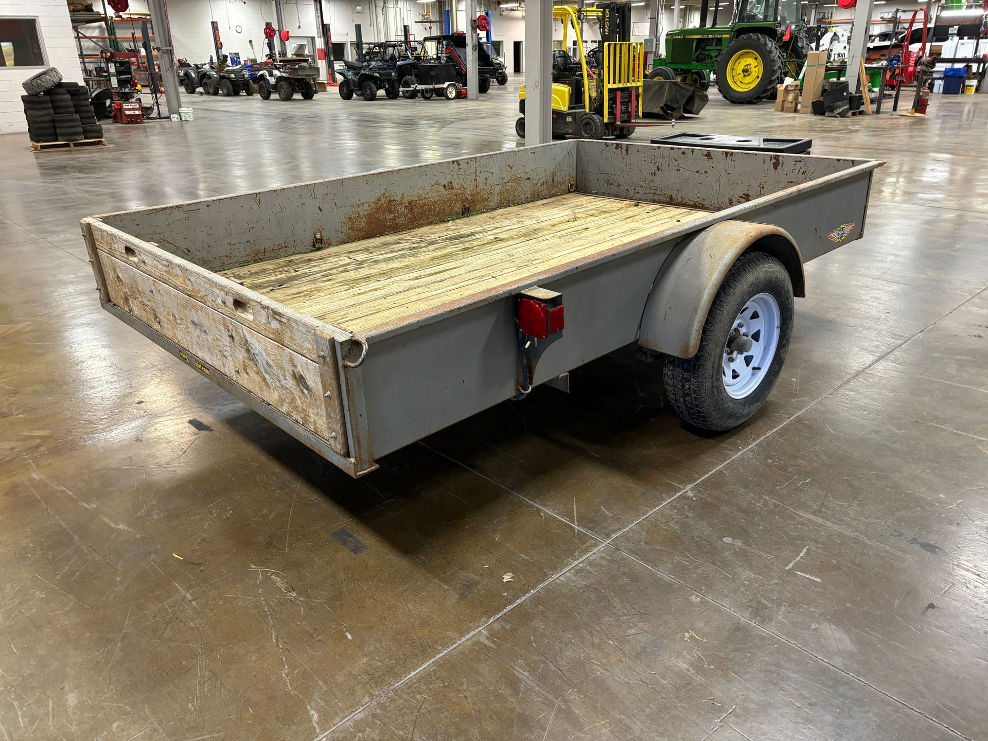 Gray utility trailer with one wheel visible, on a concrete floor.