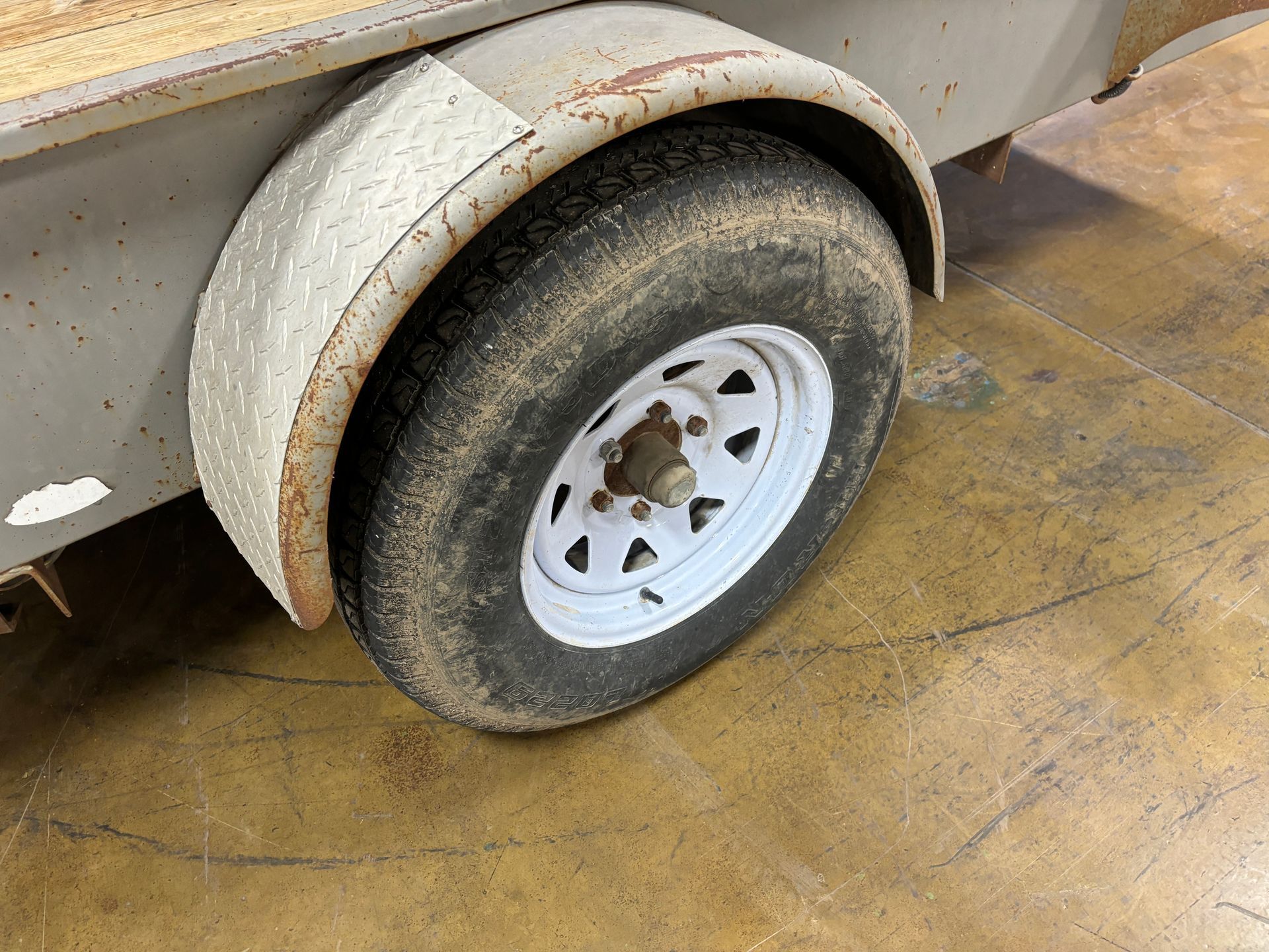 Trailer tire with a white rim and a rusted fender.