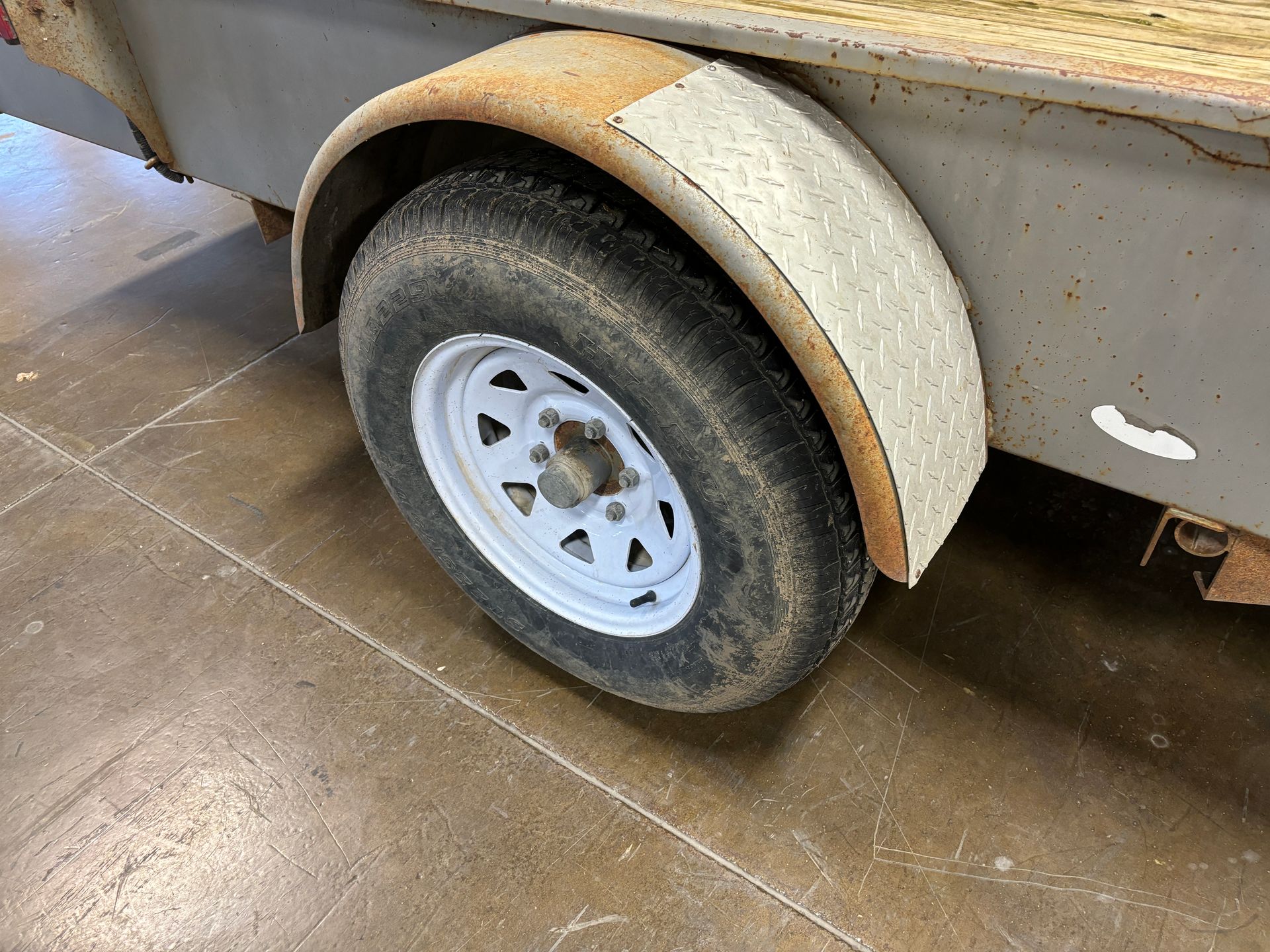 Trailer wheel with white rim and rusty fender on a concrete floor.