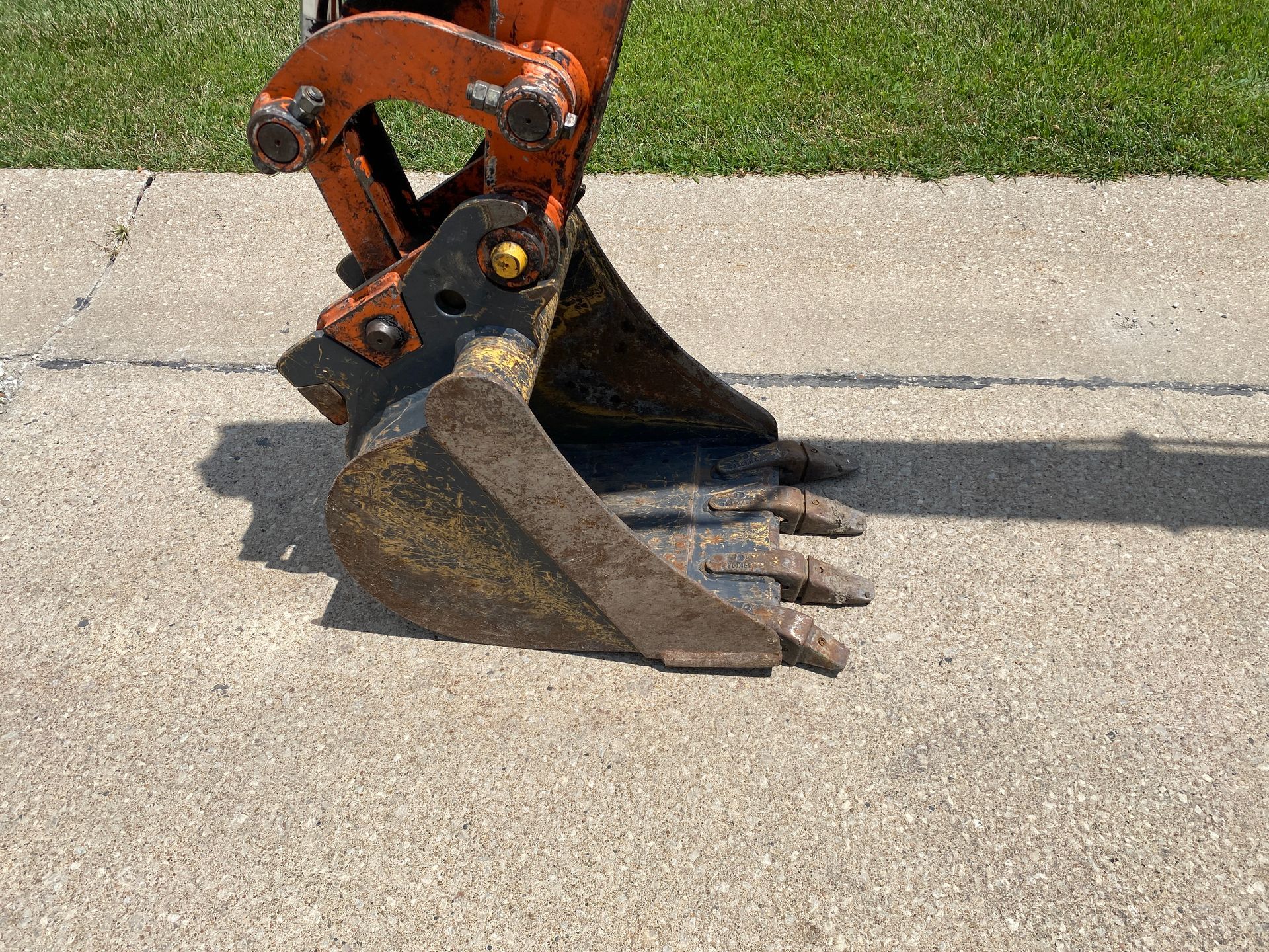 Orange Hitachi excavator arm on green grass with a tree and building in the background.