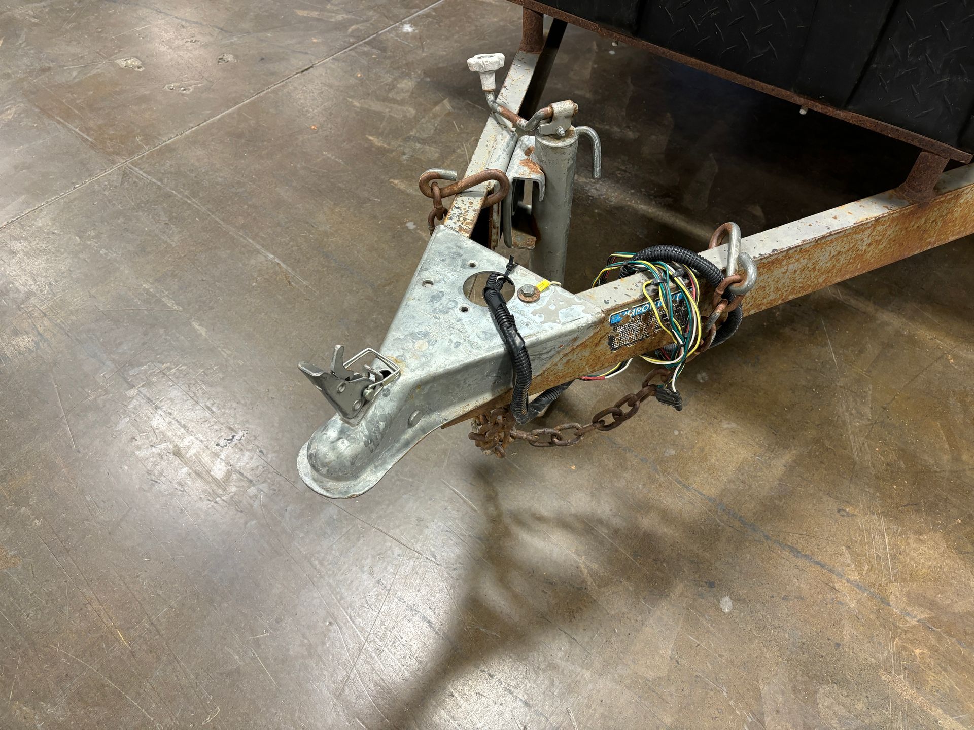 Rusty trailer hitch on a concrete floor with chains and a crank.