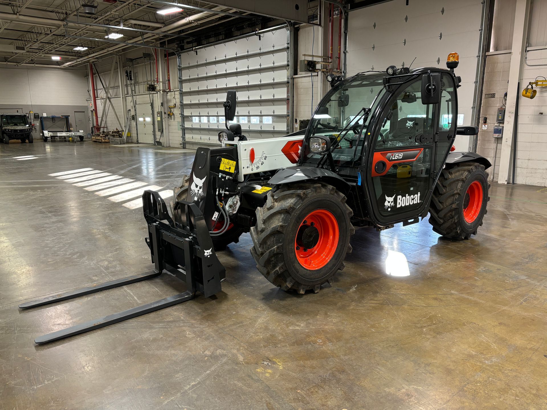 Bobcat telehandler with black and orange accents, forks extended, in a warehouse.