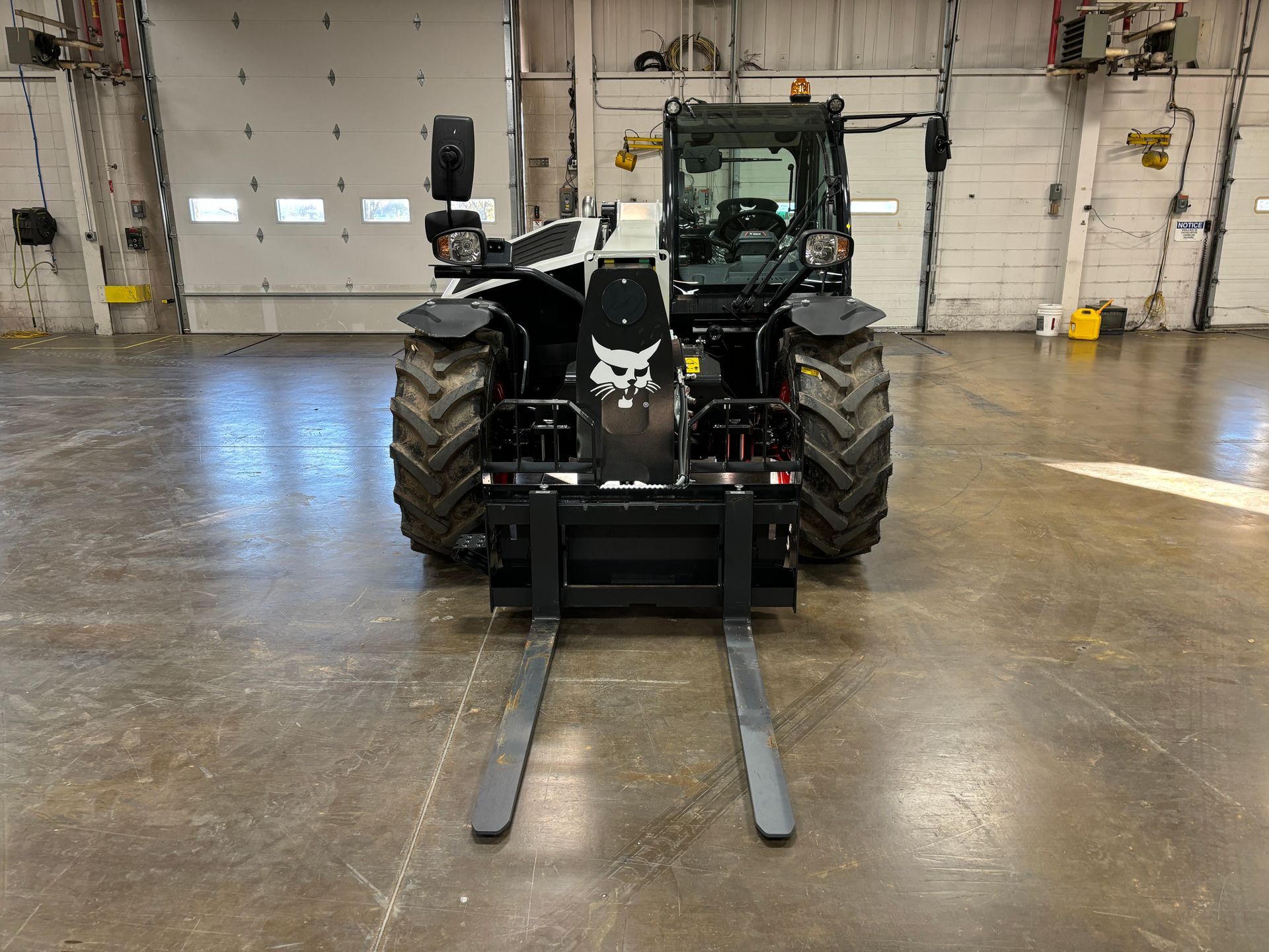 Bobcat telehandler with lowered forks, in an industrial setting.