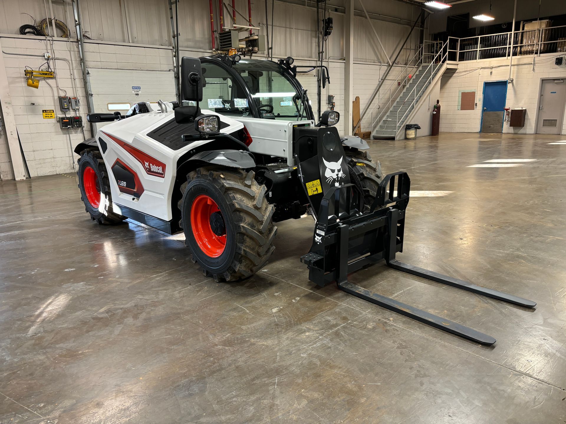 Bobcat telehandler with black forks, red wheels, and white body in a warehouse.