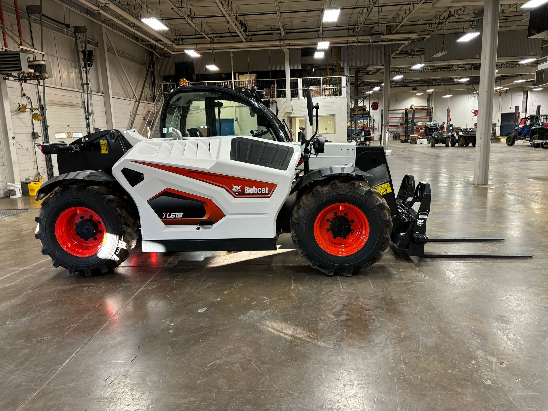 White and red Bobcat telehandler with orange wheels inside a warehouse.