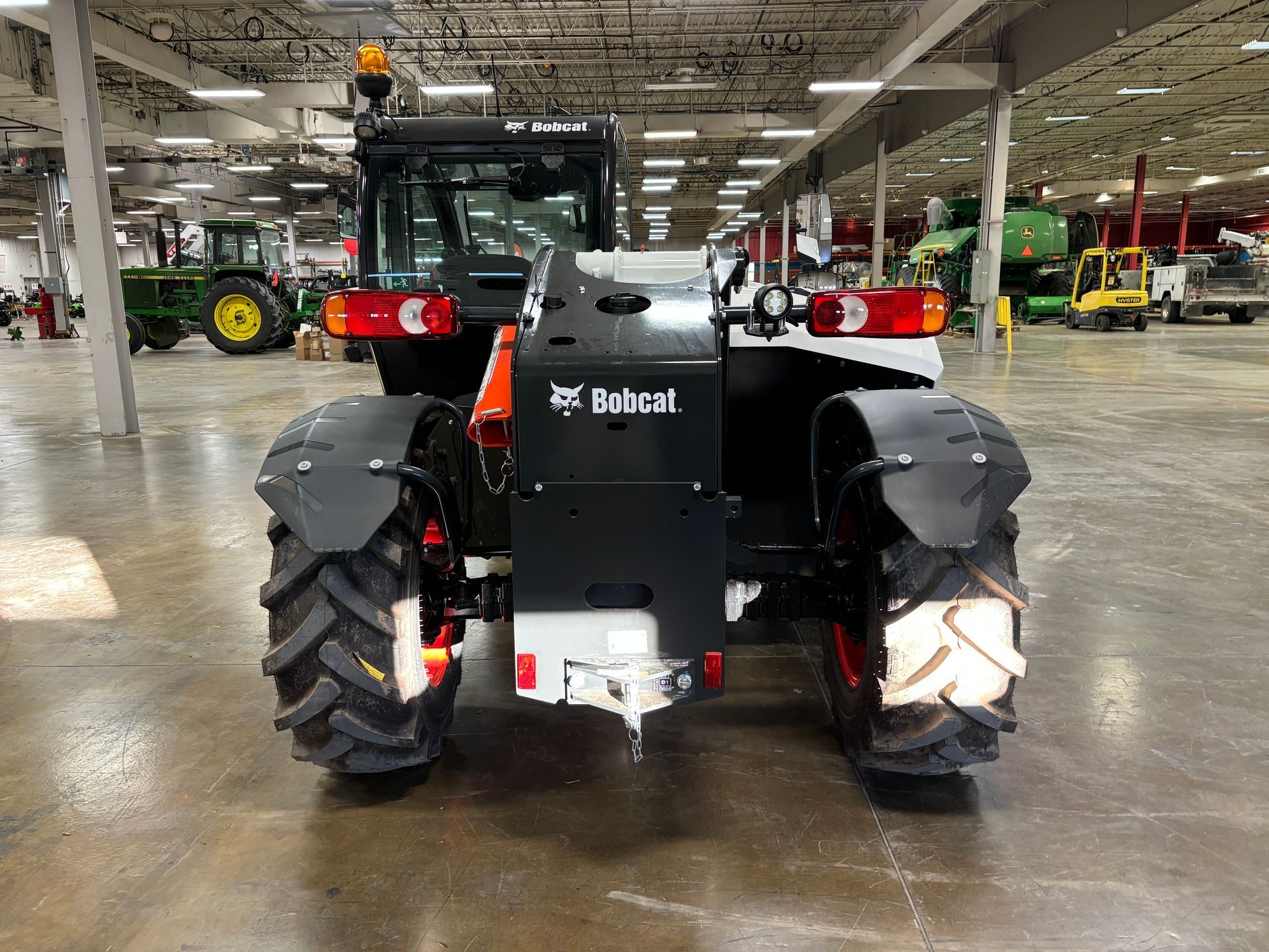 Rear view of a Bobcat tractor with black tires, orange accents, and black fenders inside a large building.