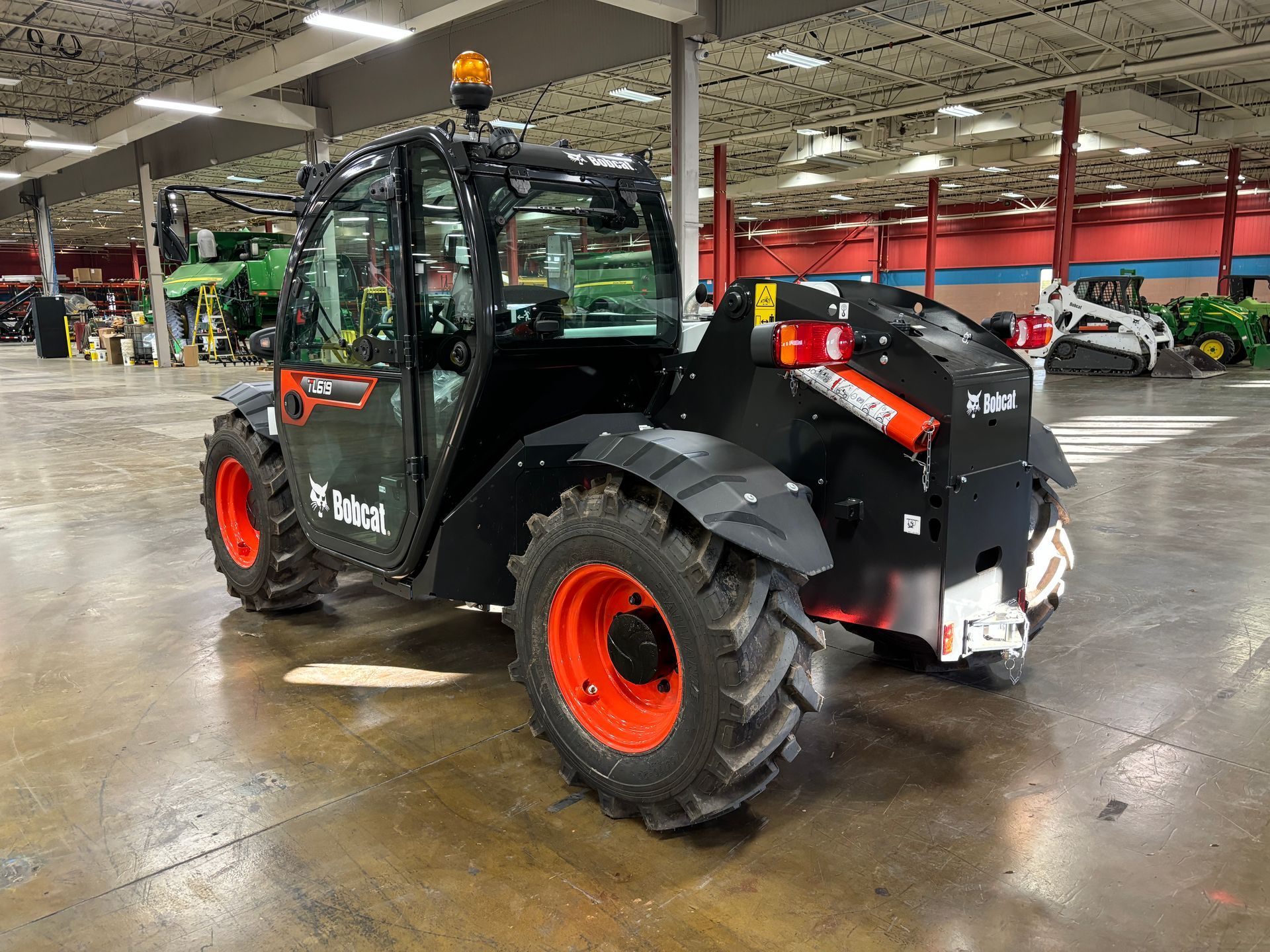 Black Bobcat telehandler with orange wheels, indoors.