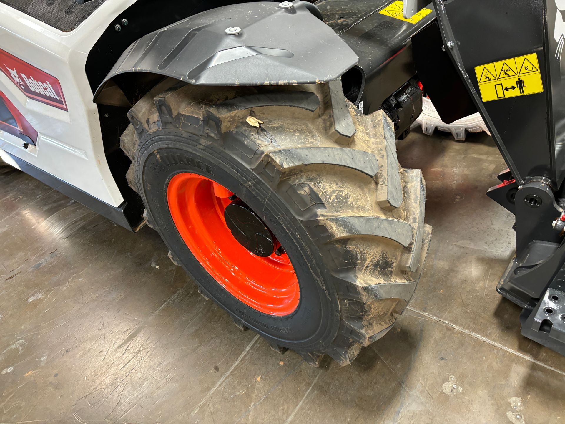 Close-up of a Bobcat skid-steer loader wheel with a black tire and orange rim, covered in dirt.