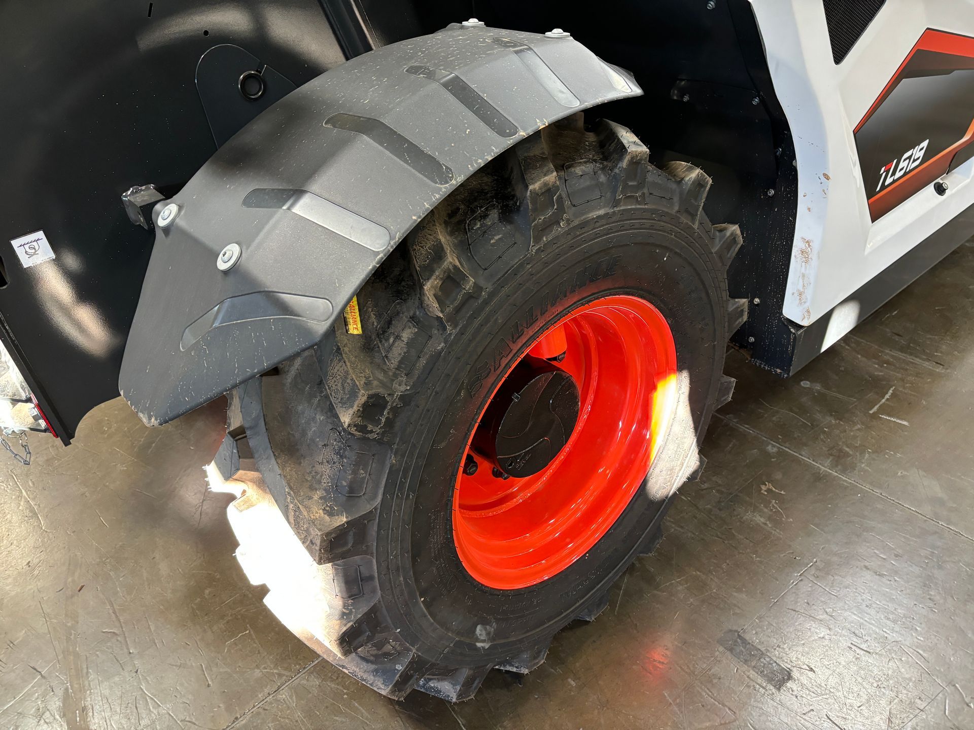 Black fender and orange wheel of a Bobcat skid-steer loader, on a concrete surface.