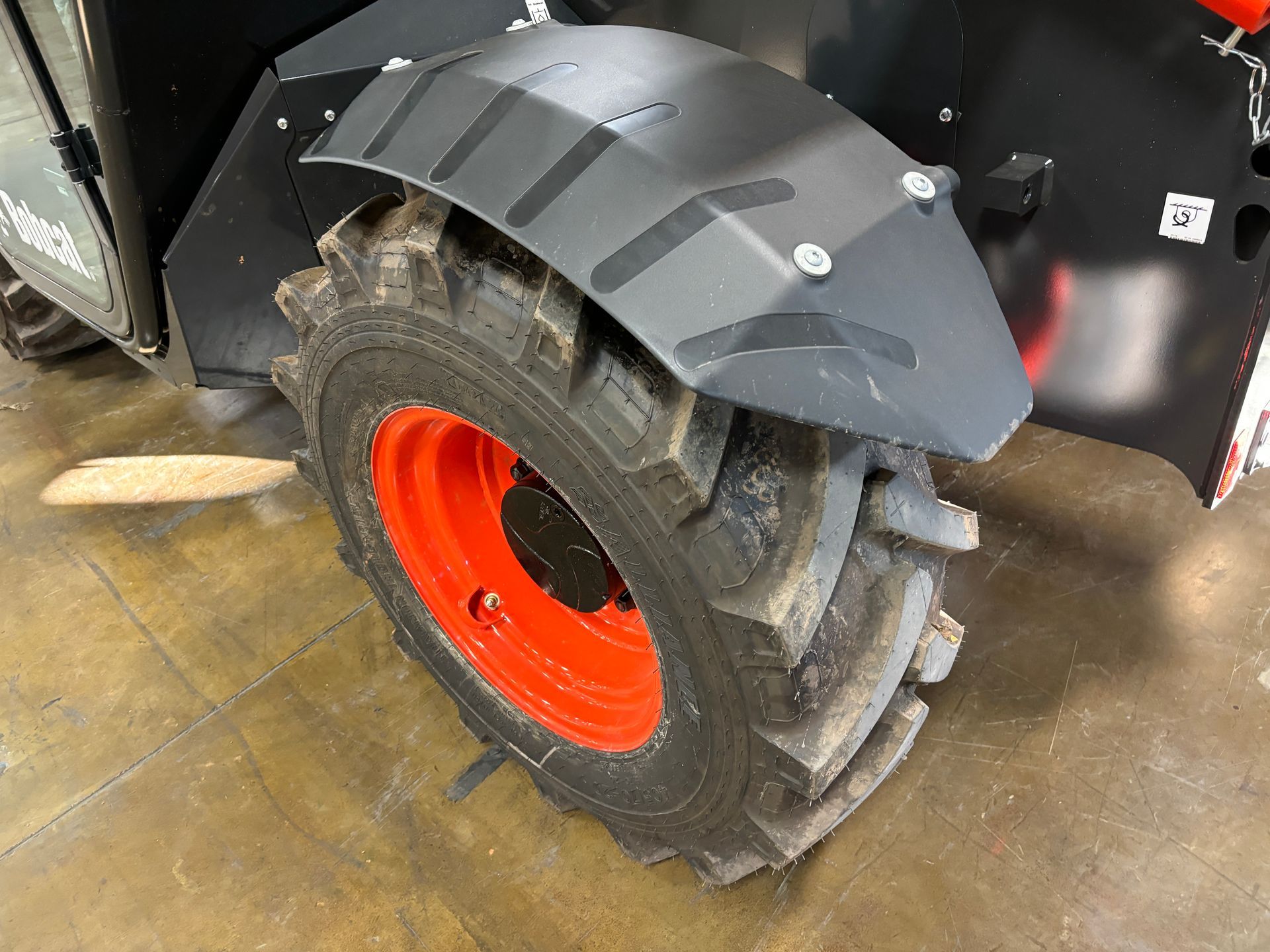 Black fender over a large, muddy tire with a red rim, attached to a black machine.