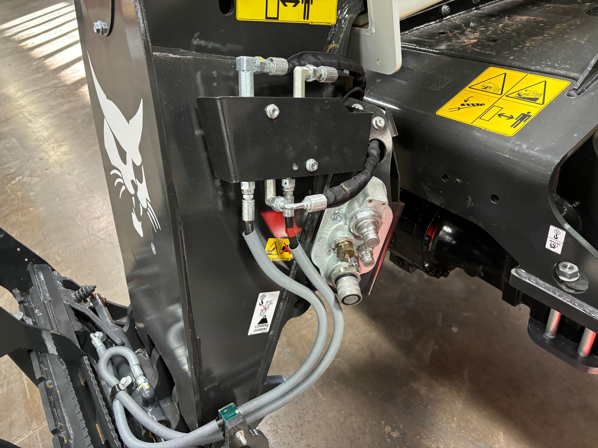 Close-up of Bobcat machine hydraulics: black metal, gray hoses, yellow and red levers.
