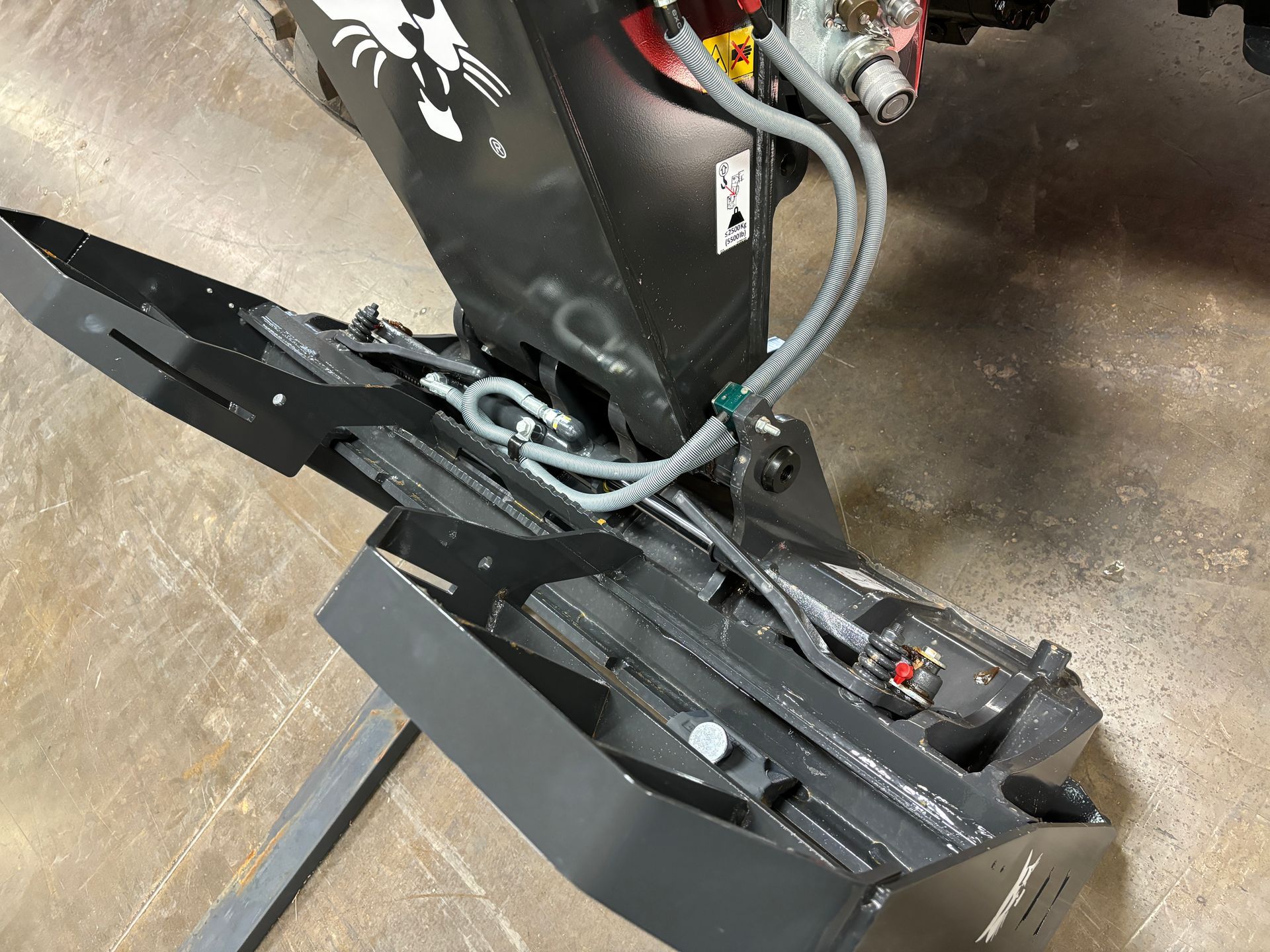 Black and grey Bobcat forestry cutter attachment, with hoses and sharp blades, viewed from above.
