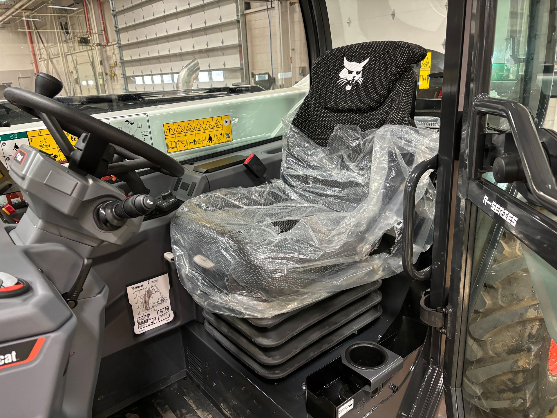 Interior of a Bobcat construction vehicle with a seat covered in plastic, steering wheel, and control panel.
