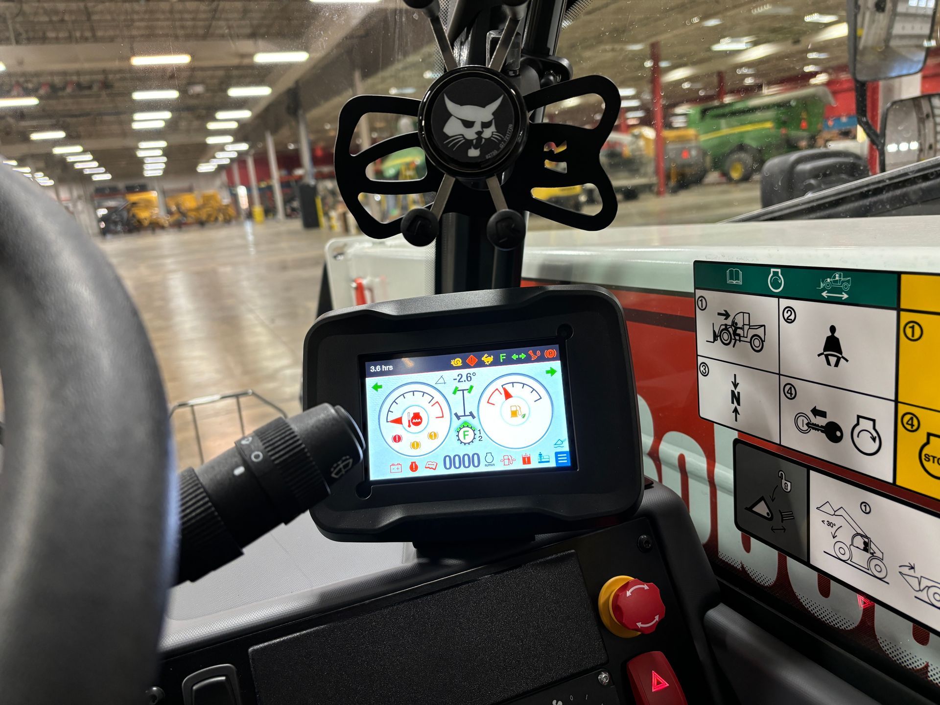 Dashboard of a Bobcat heavy machinery, with a digital display showing gauges. Red emergency stop button visible.