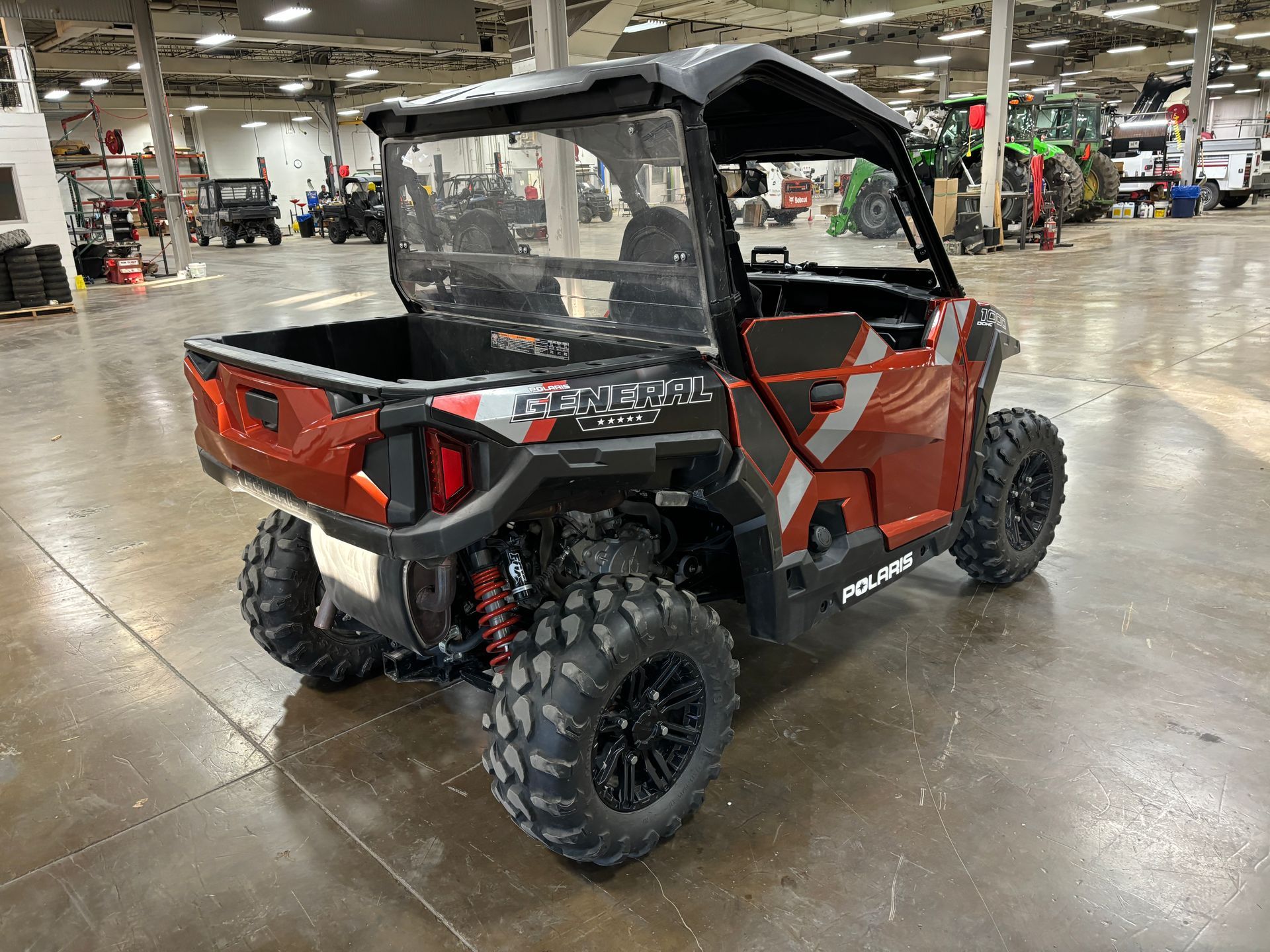 Red Polaris General UTV with black roof, large tires, and clear back panel in a showroom.