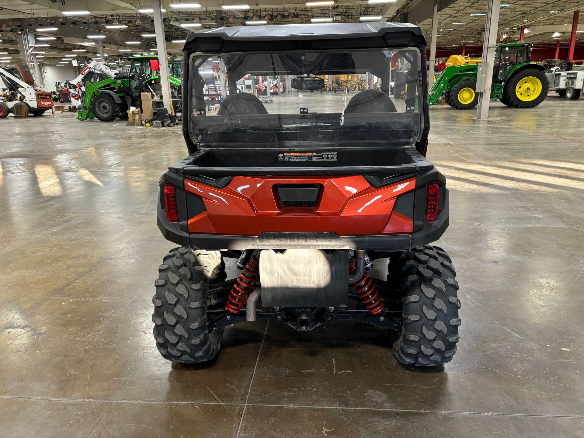 Rear view of an orange and black off-road vehicle with large tires in a warehouse.