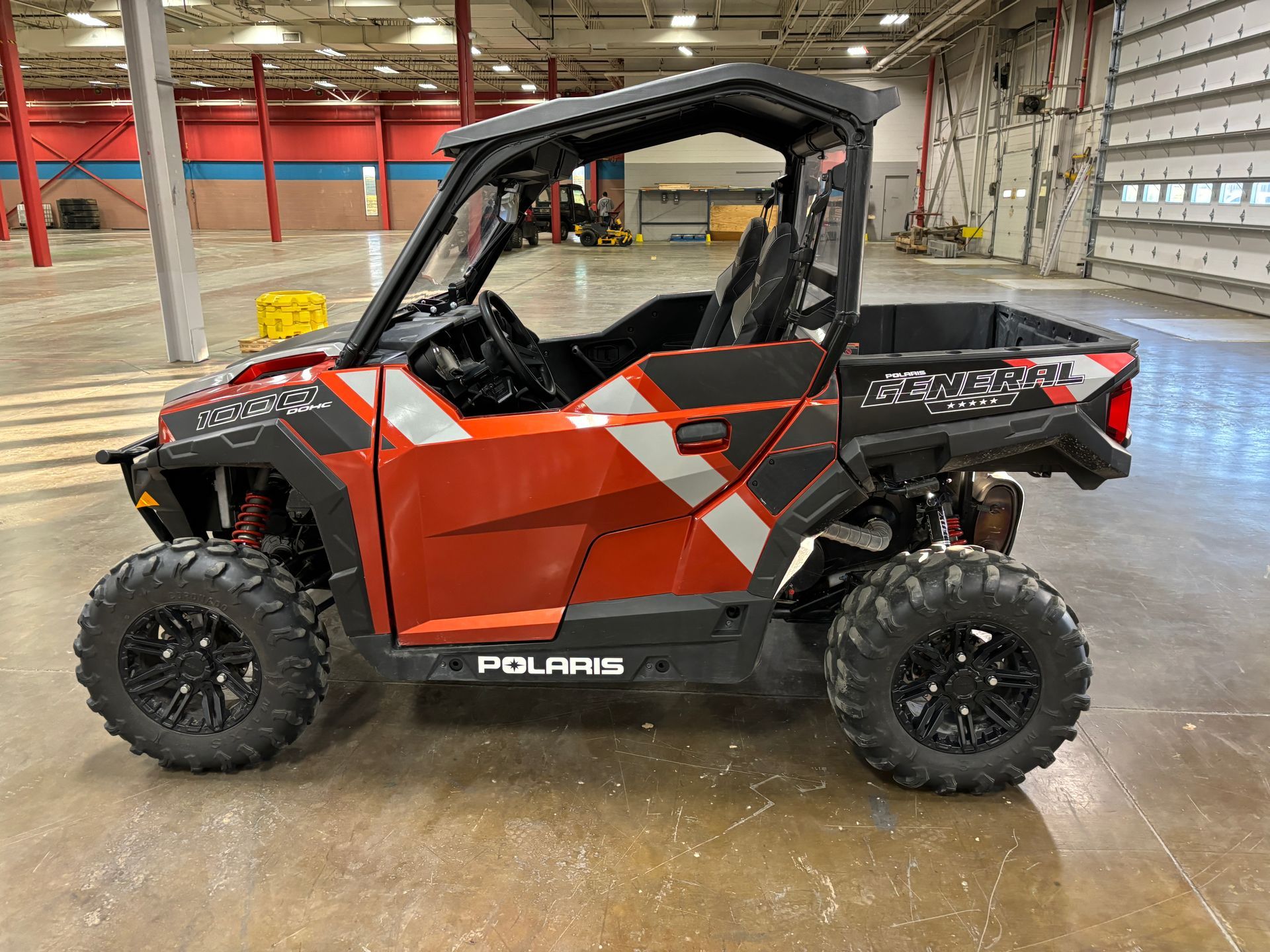 Red and black Polaris General side-by-side vehicle with black wheels, parked indoors.