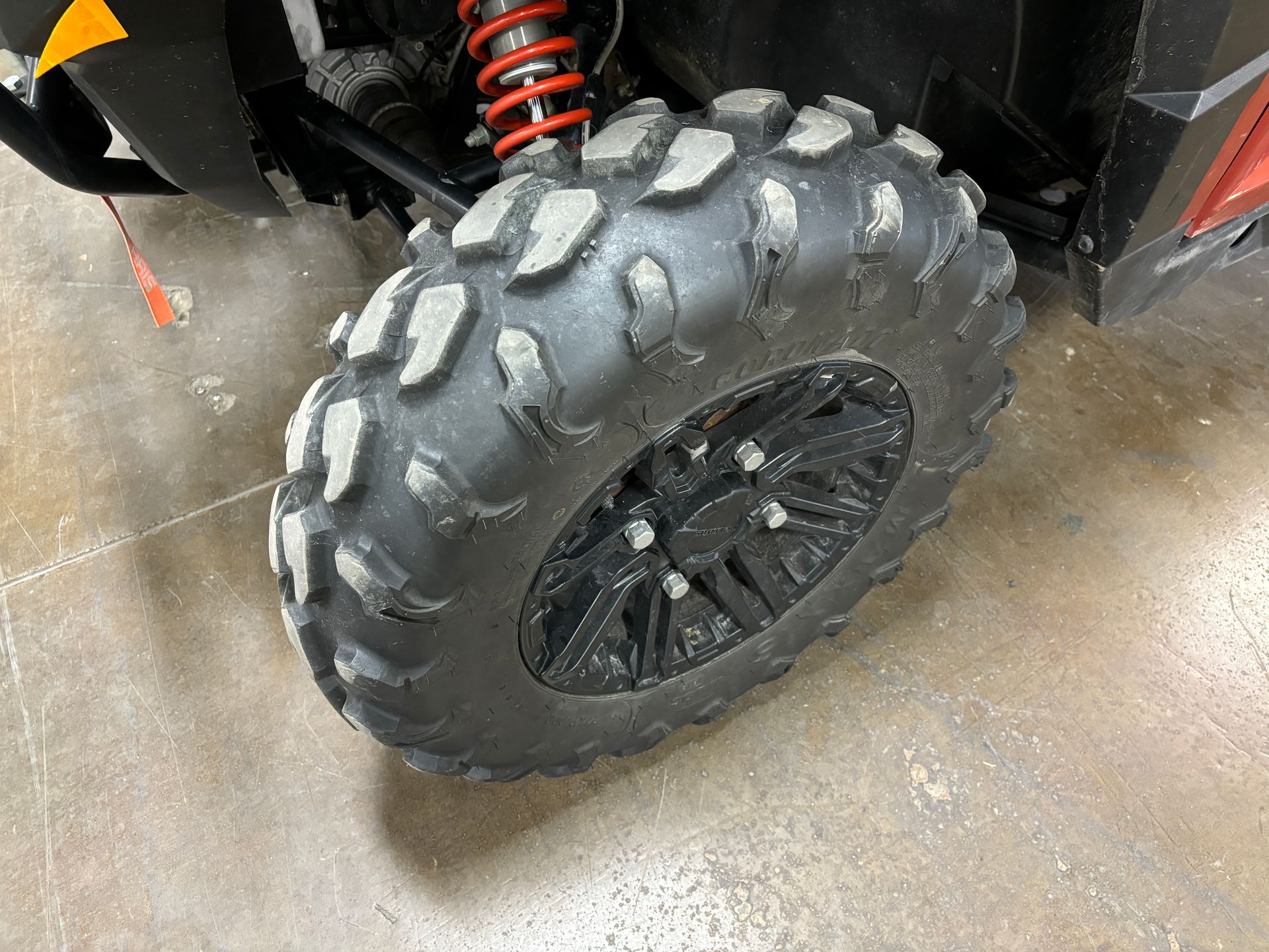 Black UTV tire with thick tread on a black wheel, parked on a concrete floor.