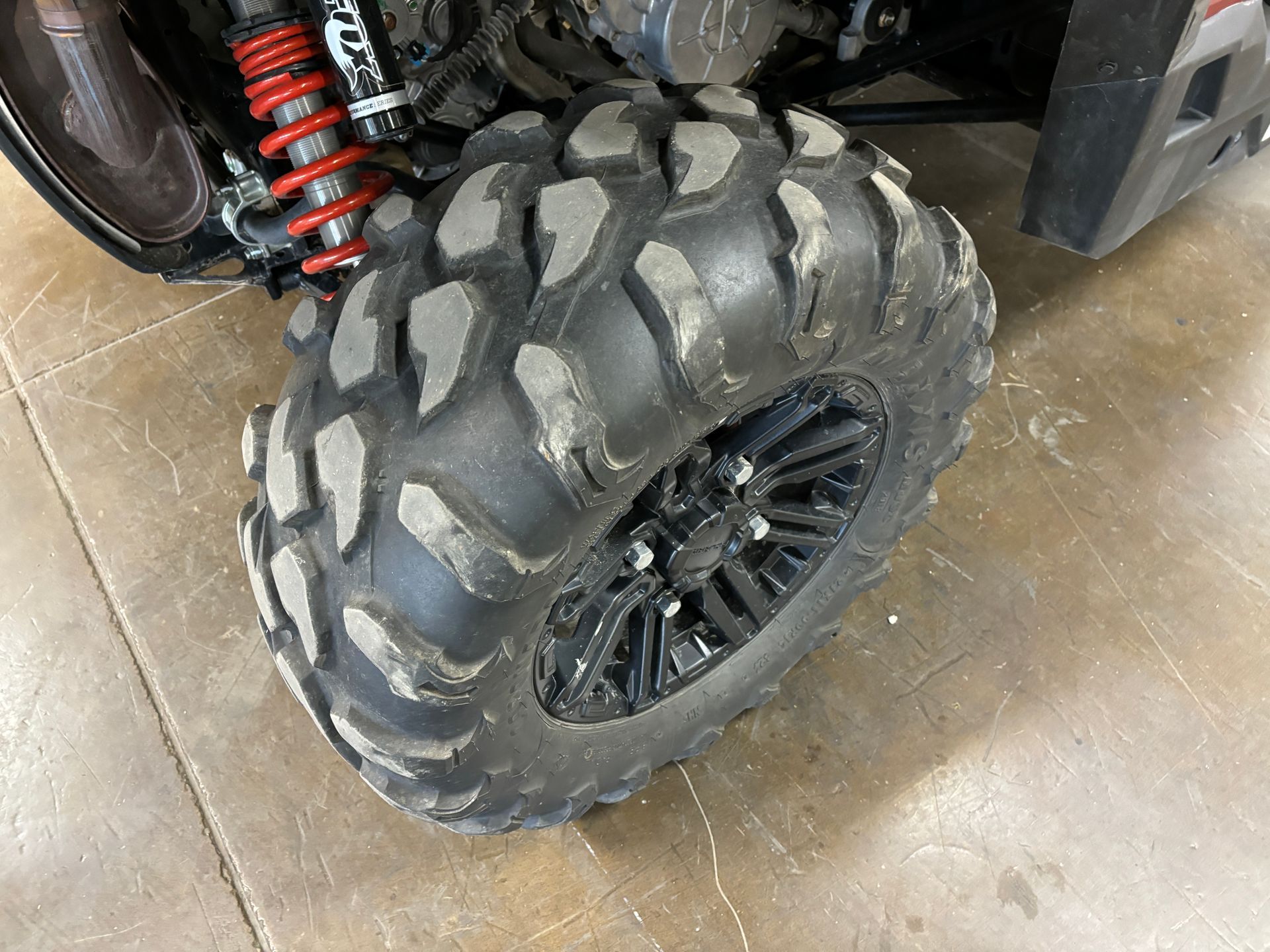 Black all-terrain tire on a black wheel. The suspension spring is red.