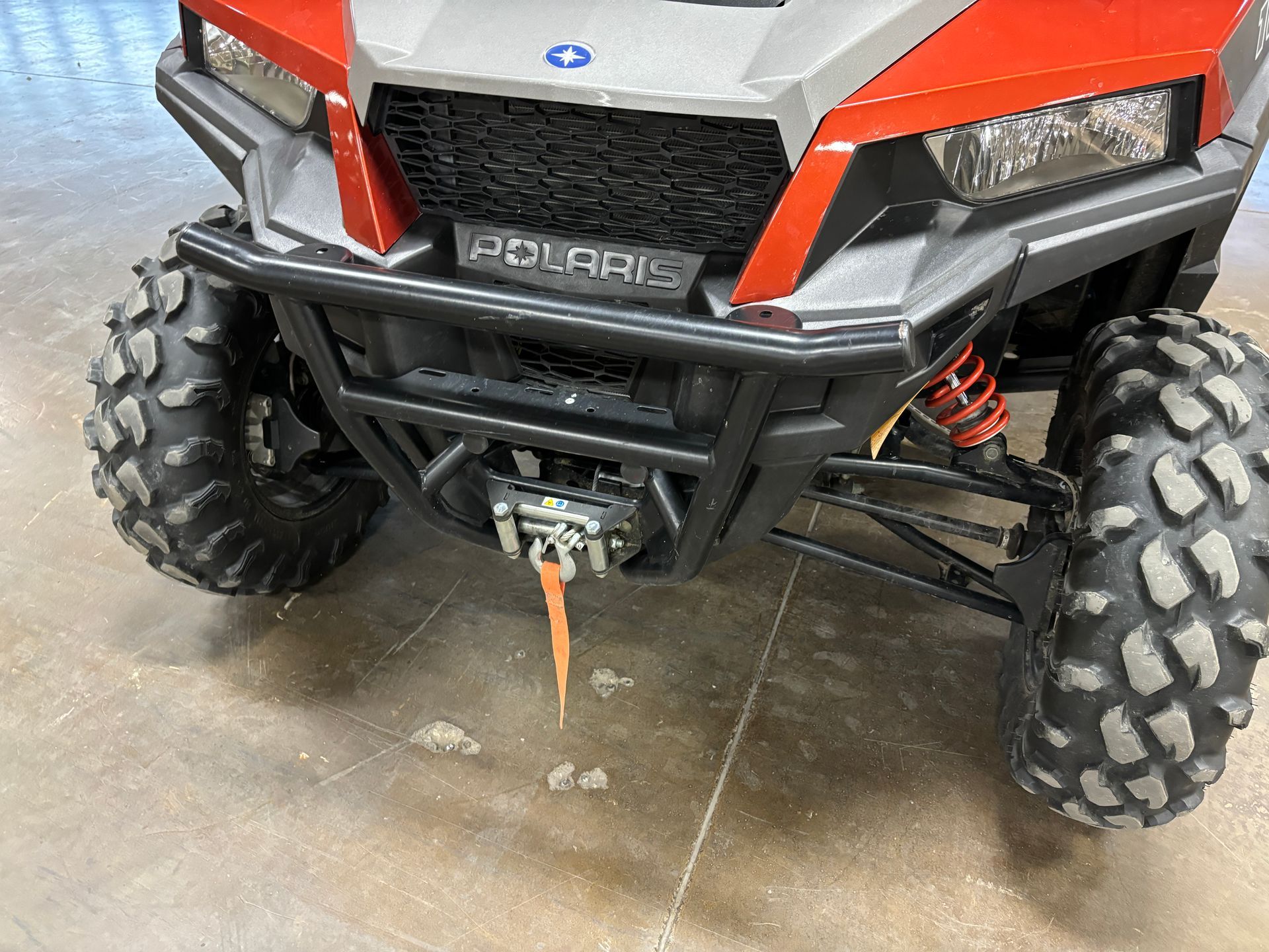 Red and gray Polaris off-road vehicle with large black tires, front-facing.