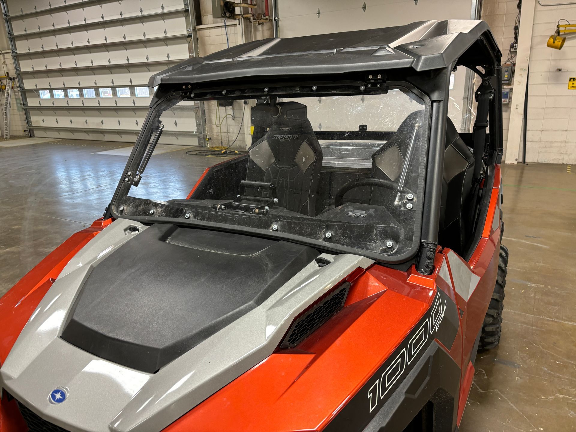 Red and gray Polaris General UTV with a windshield inside a garage.
