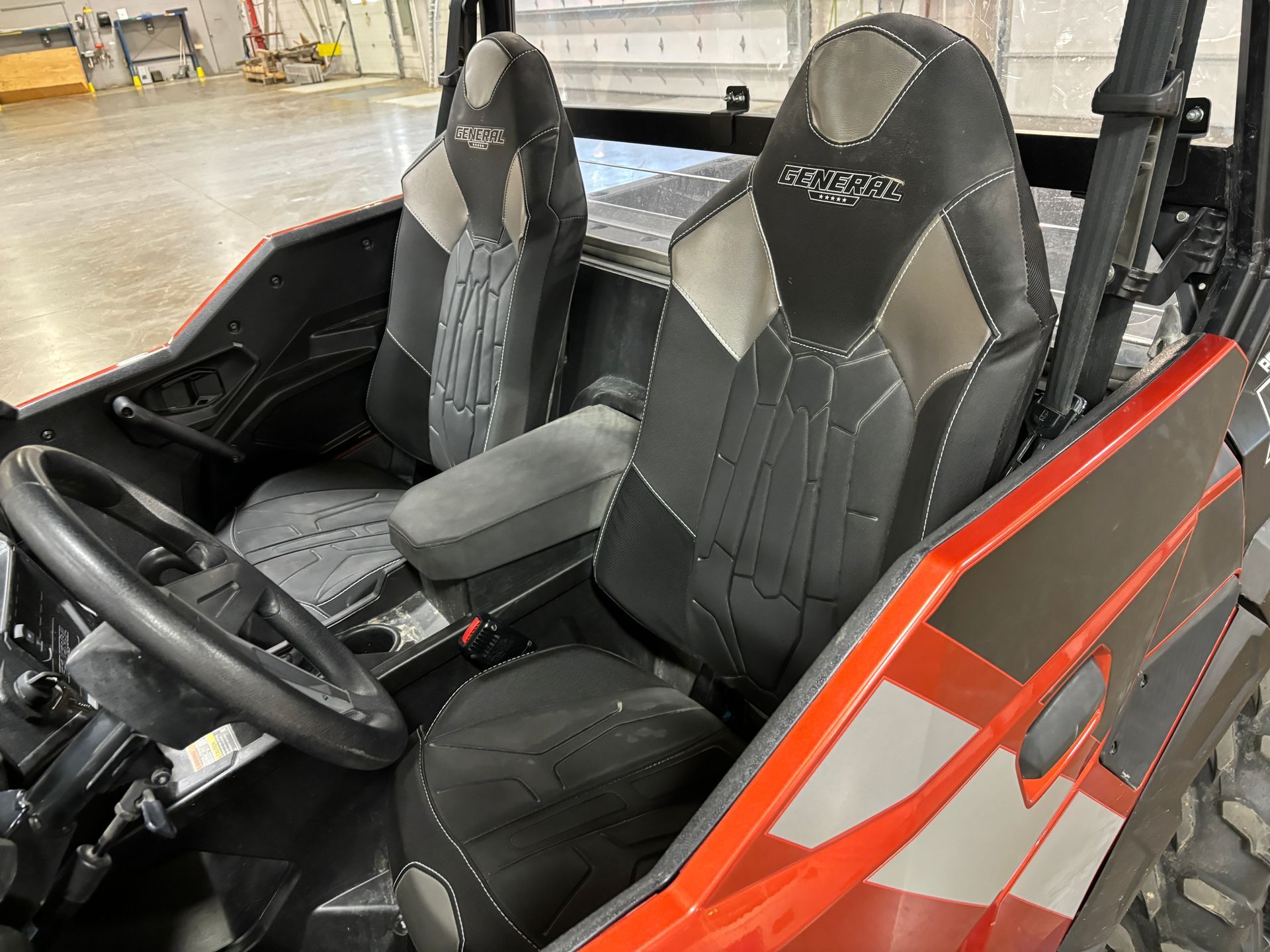 Interior of an orange UTV with two black and gray seats and a black steering wheel.