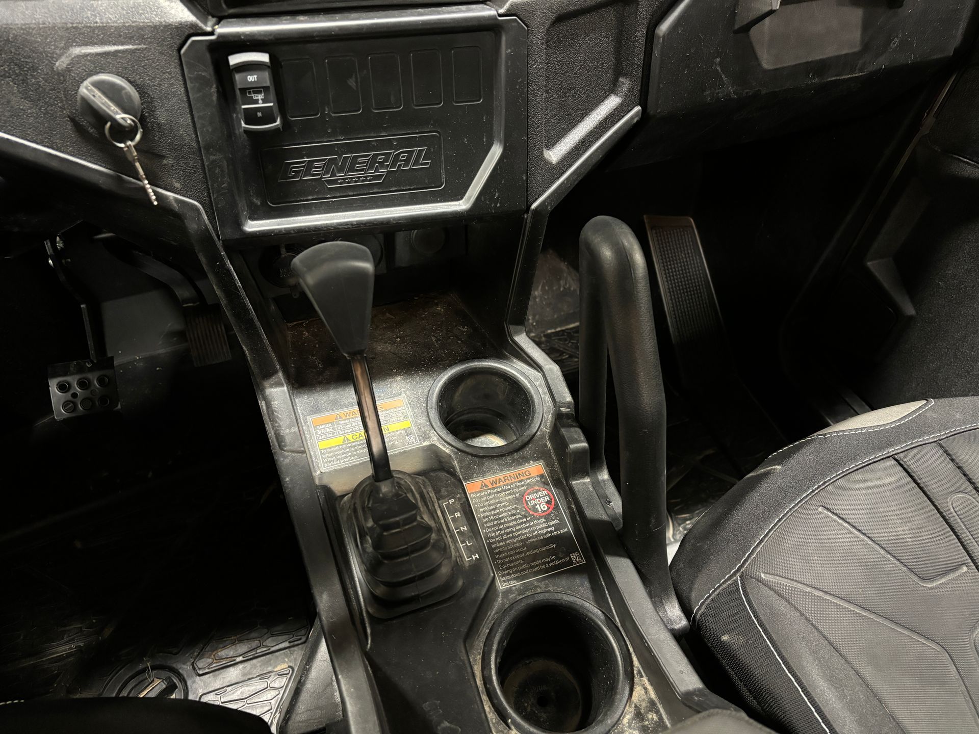 Interior of a UTV with a gear shift, cup holders, and radio panel.