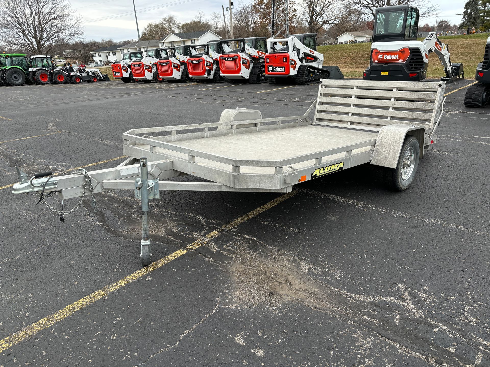Aluminum utility trailer in a parking lot, with construction equipment visible in the background.