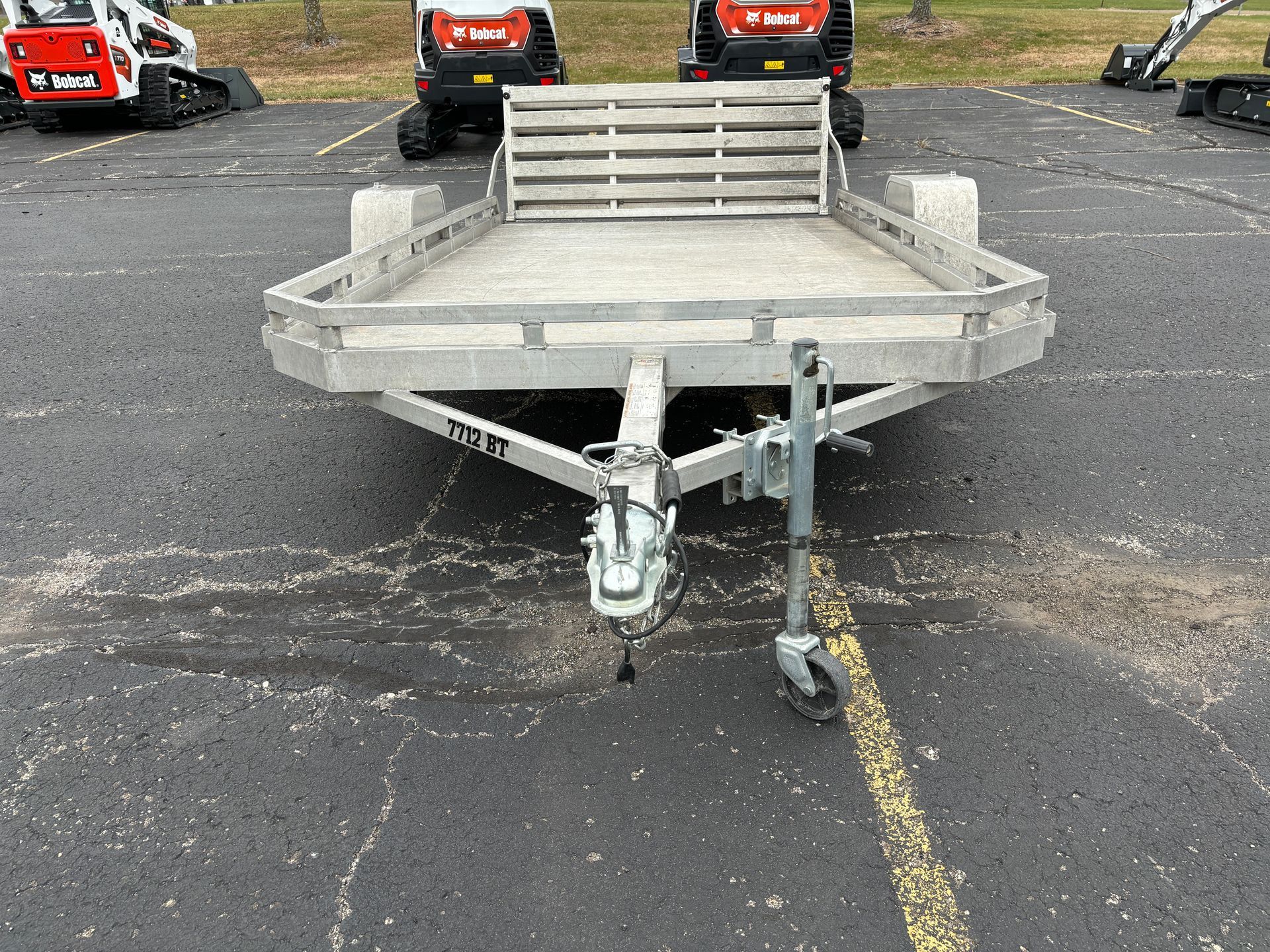 An aluminum trailer with a wooden gate, parked on asphalt.