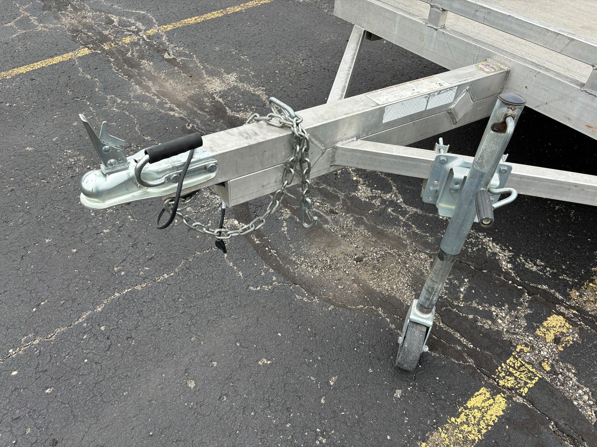 Trailer hitch with safety chains and jack on asphalt.