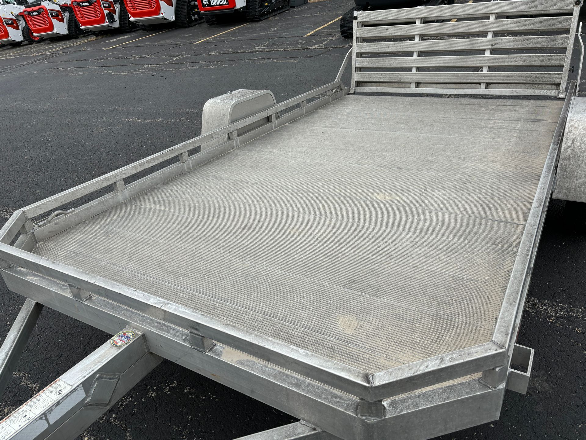 Aluminum flatbed utility trailer with corrugated surface and wood-slat headboard.
