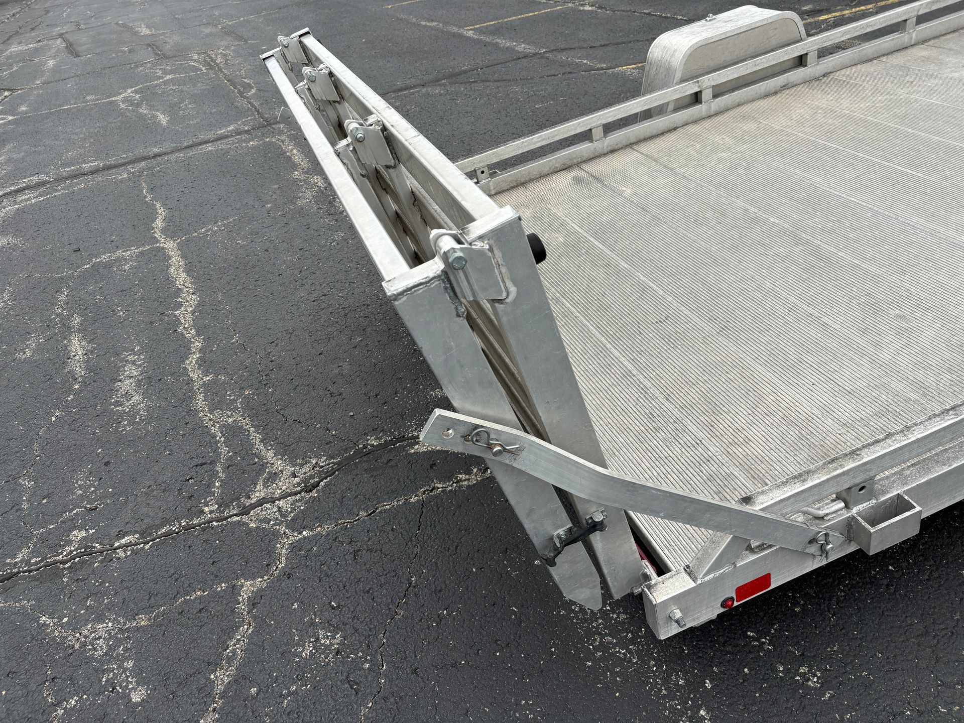 Aluminum trailer with ramp down on cracked asphalt.