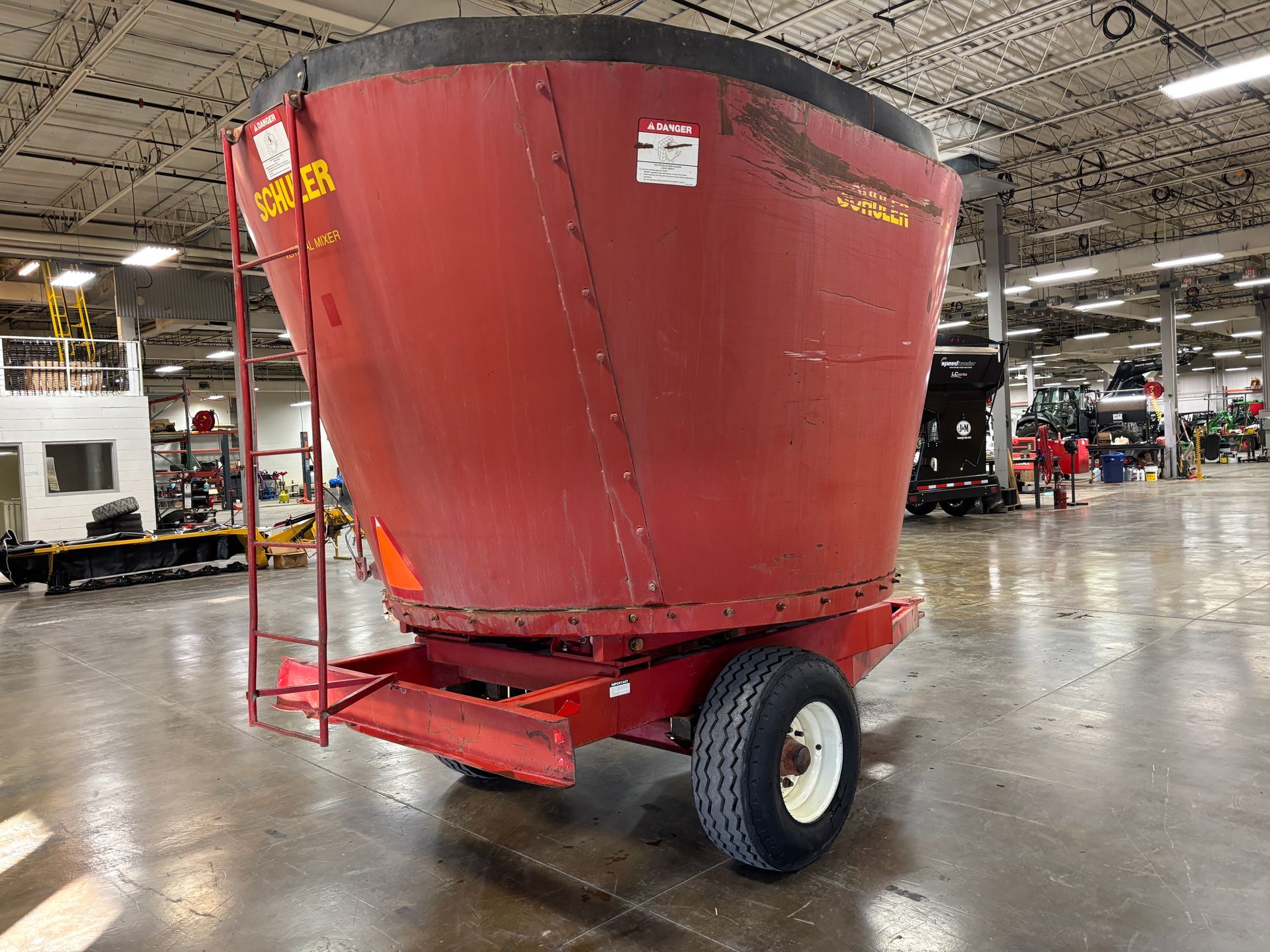 Red mixer wagon with SCHULER branding, parked inside a warehouse, back angled shot.