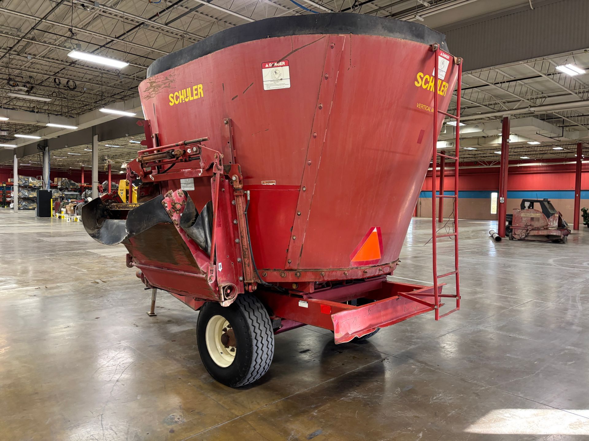 Red mixer wagon with SCHULER branding, parked inside a warehouse, back angled shot.