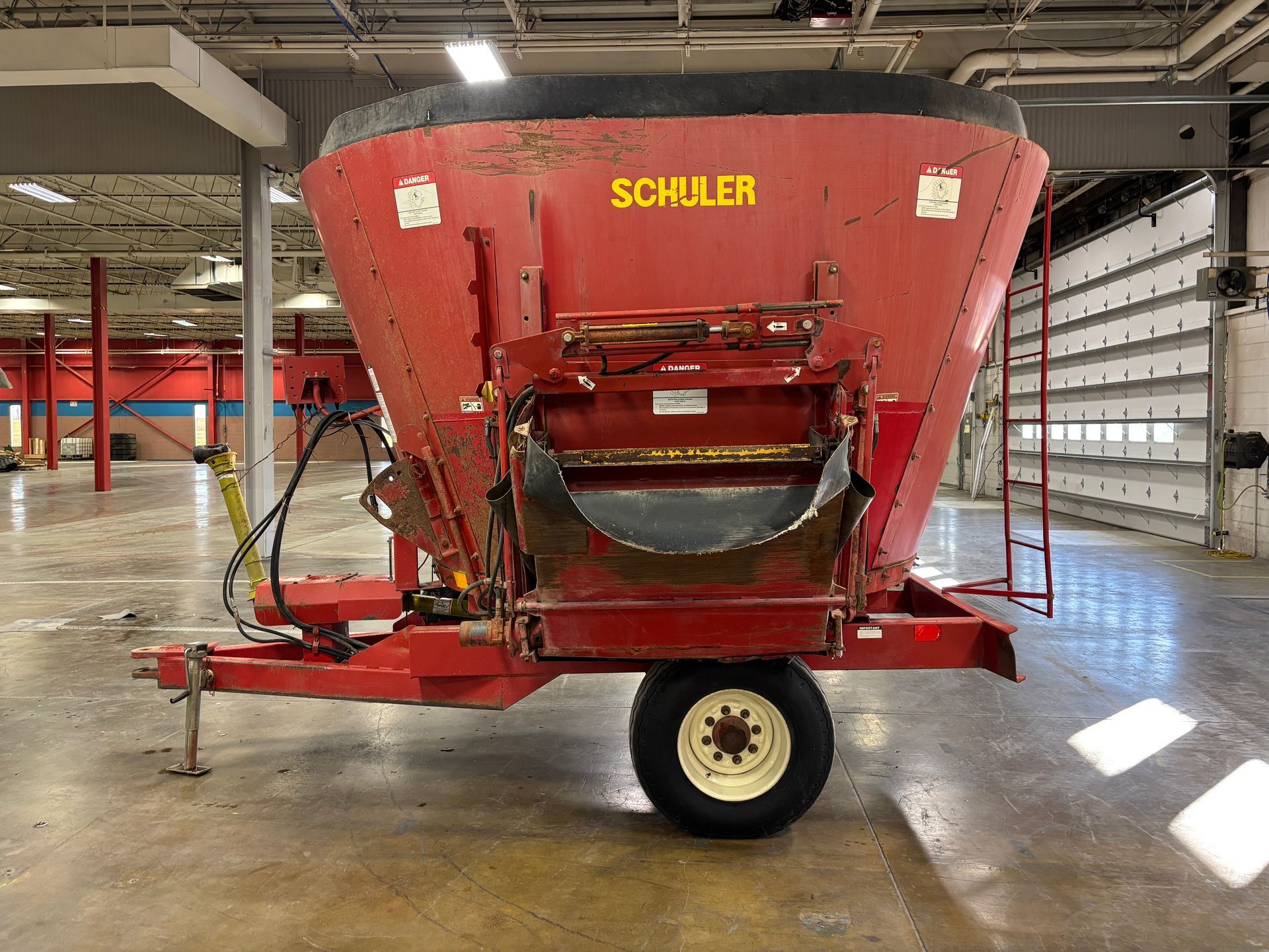 Red mixer wagon with SCHULER branding, parked inside a warehouse, side view shot.