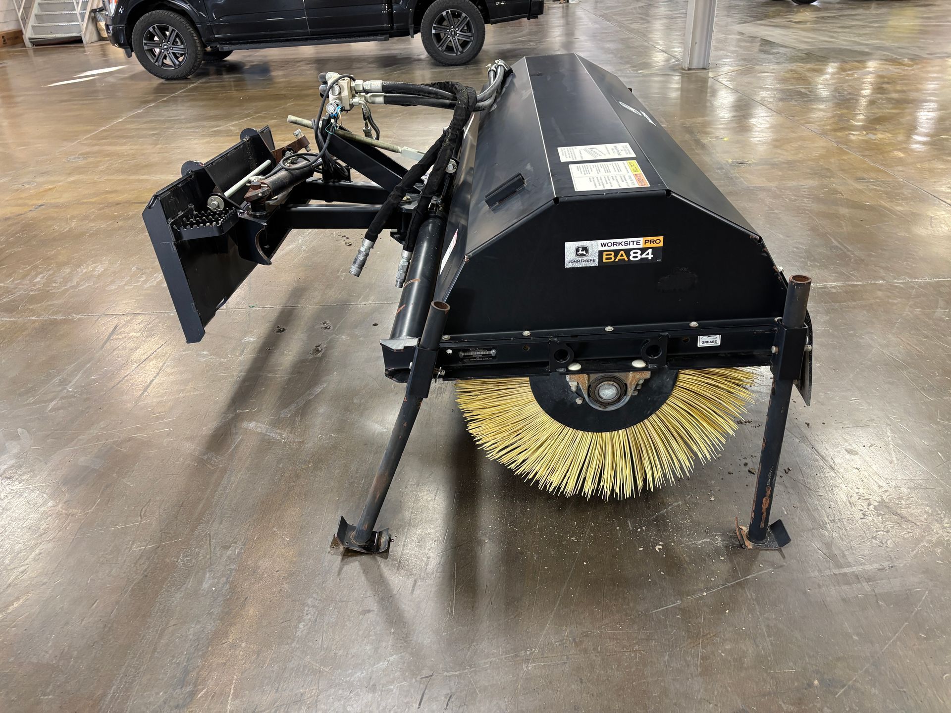 Black John Deere angle broom with yellow bristles on a concrete floor at a sideview