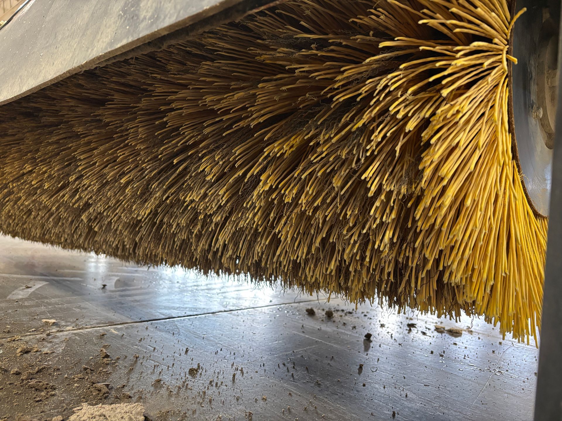 A close up shot of a black John Deere angle broom with a yellow bristles.