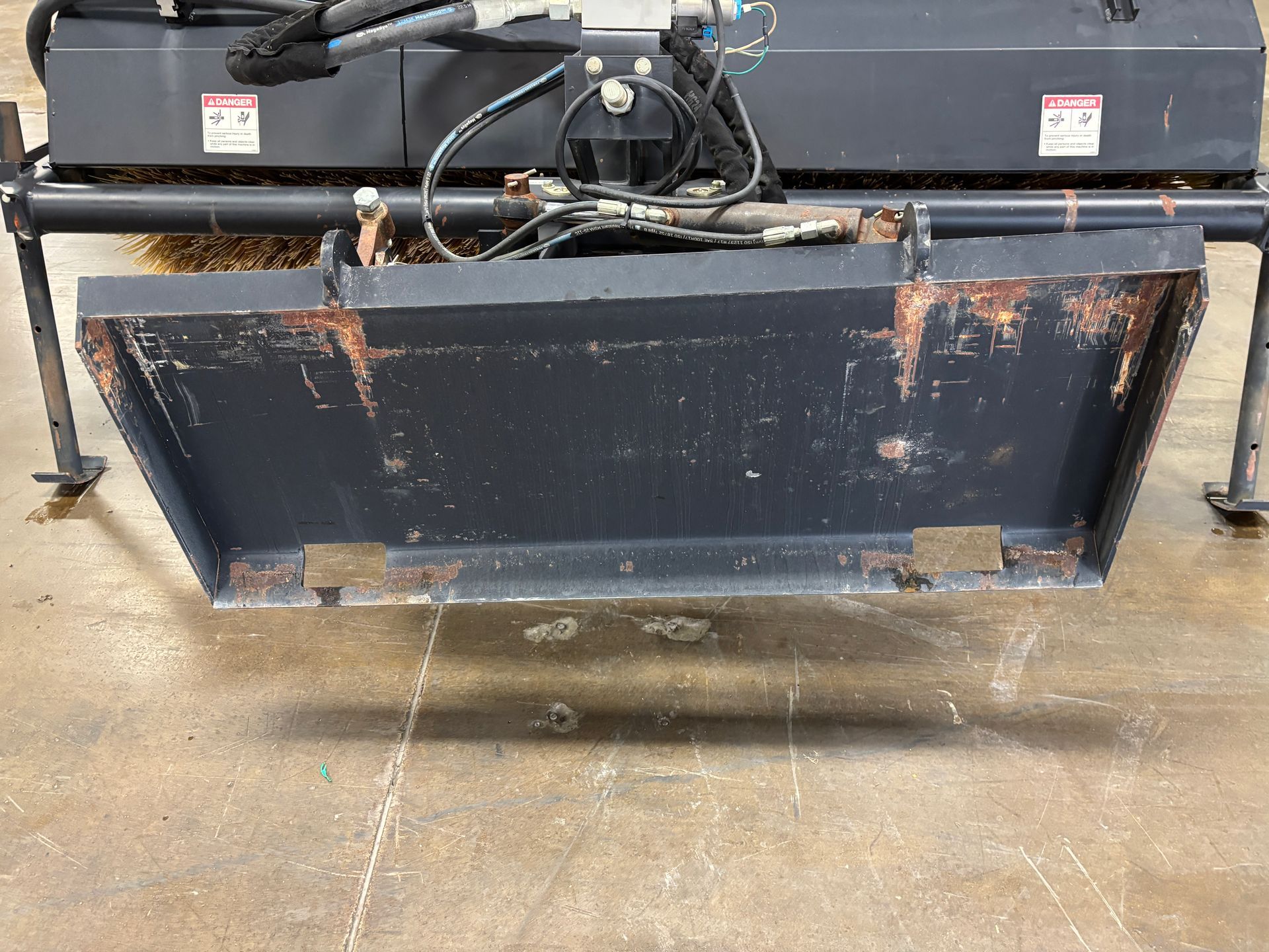Black John Deere angle broom with yellow bristles on a concrete floor.