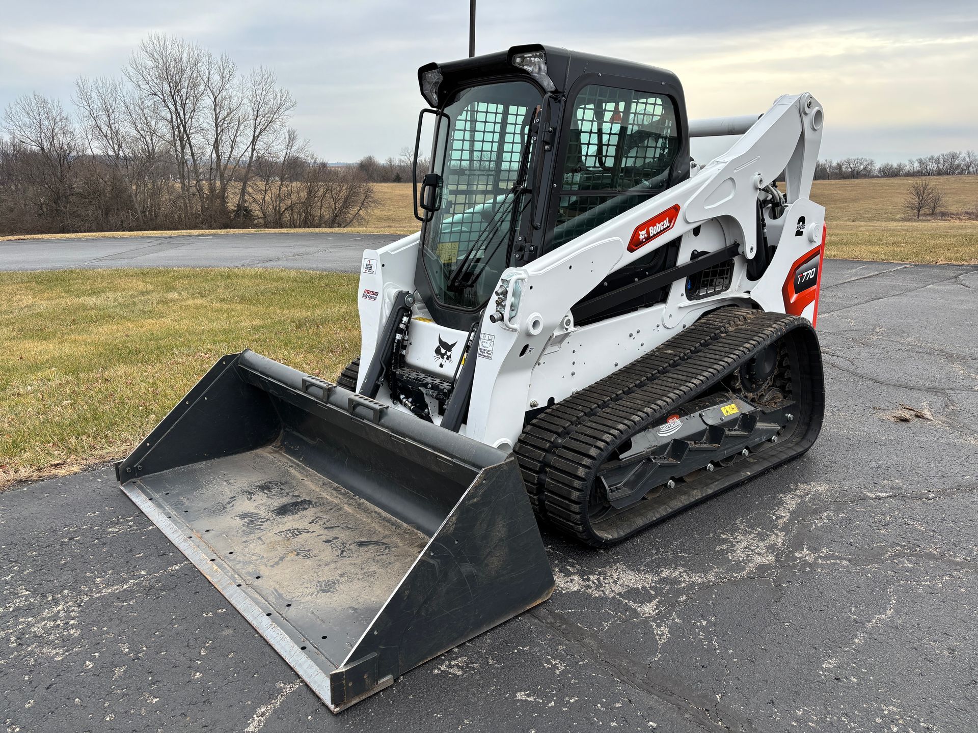 White and black Bobcat compact track loader with a bucket, outdoors on pavement, front angled shot.