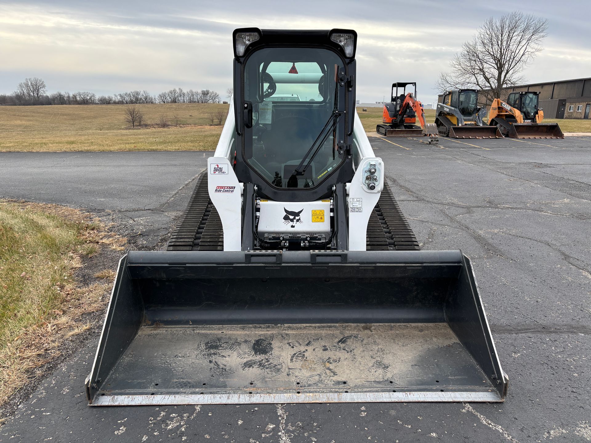 White and black Bobcat compact track loader with a bucket, outdoors on pavement, front shot.