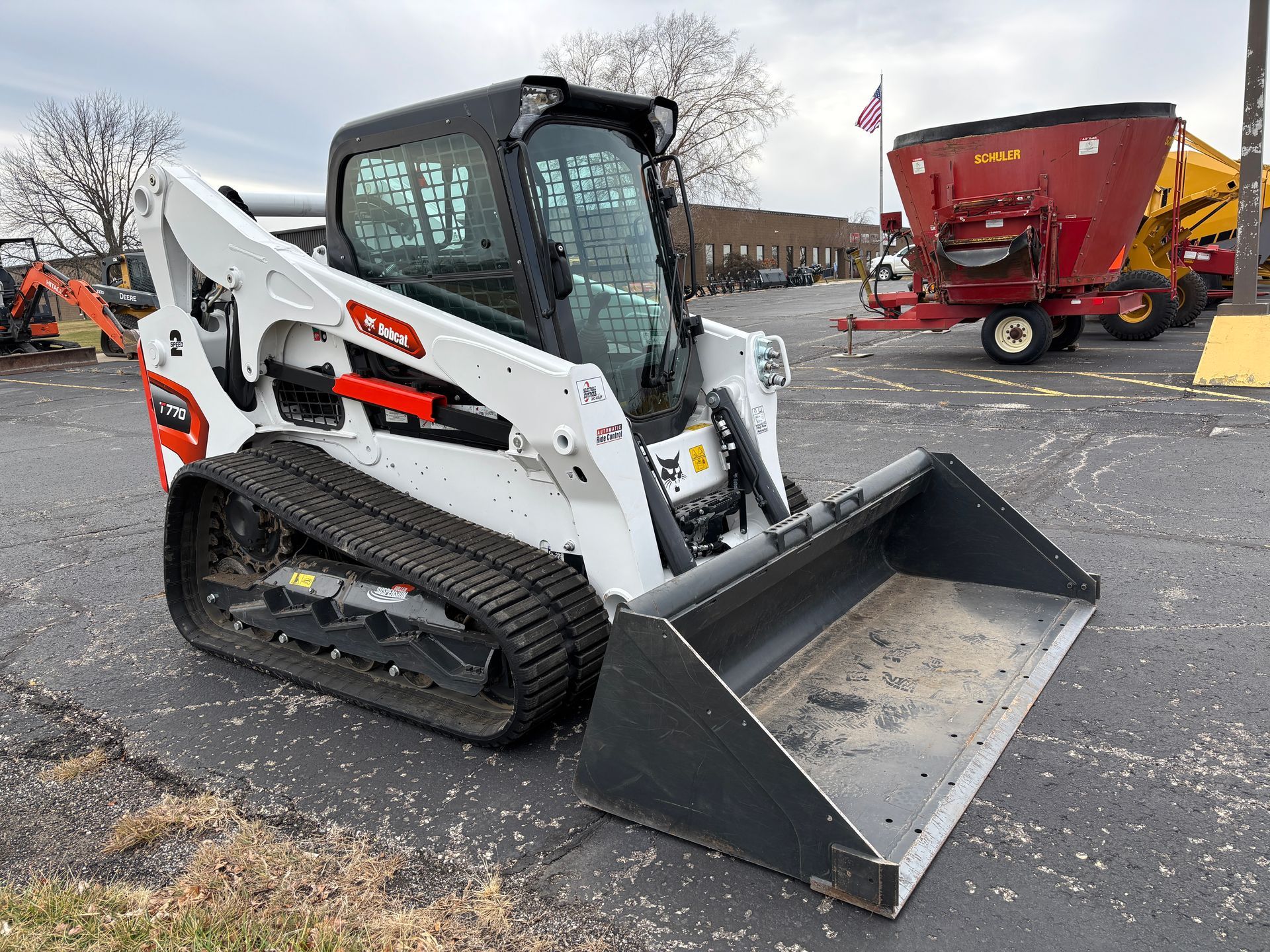 White and black Bobcat compact track loader with a bucket, outdoors on pavement, front angled shot.