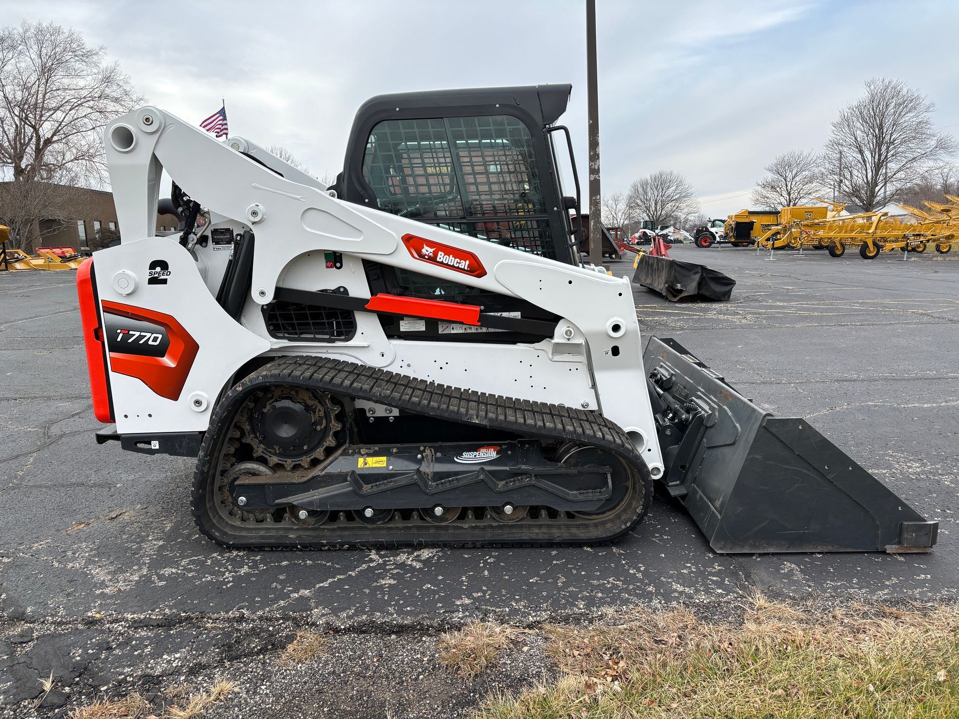 White and black Bobcat compact track loader with a bucket, outdoors on pavement, side view shot.