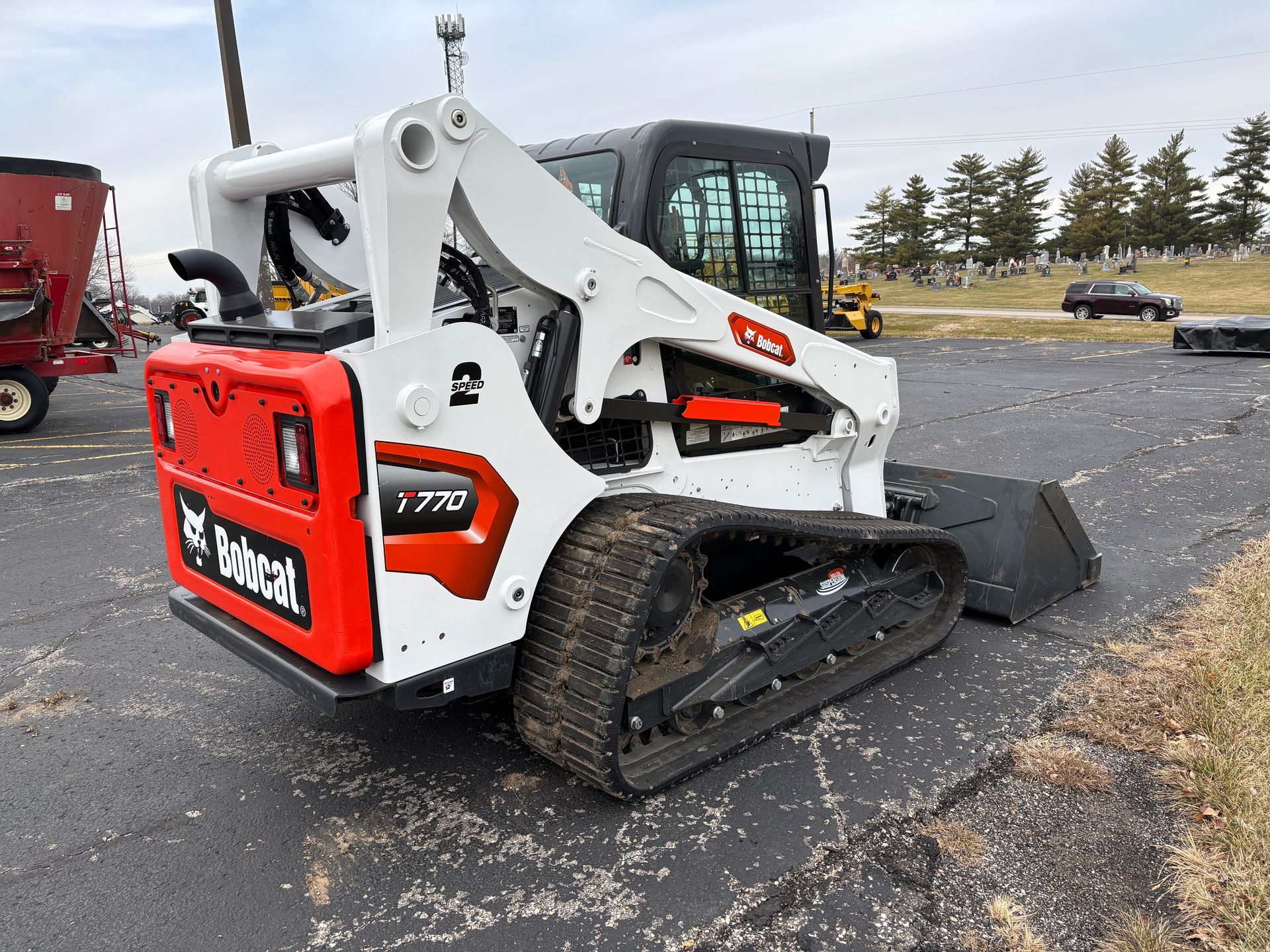 White and black Bobcat compact track loader with a bucket, outdoors on pavement, back angled shot.