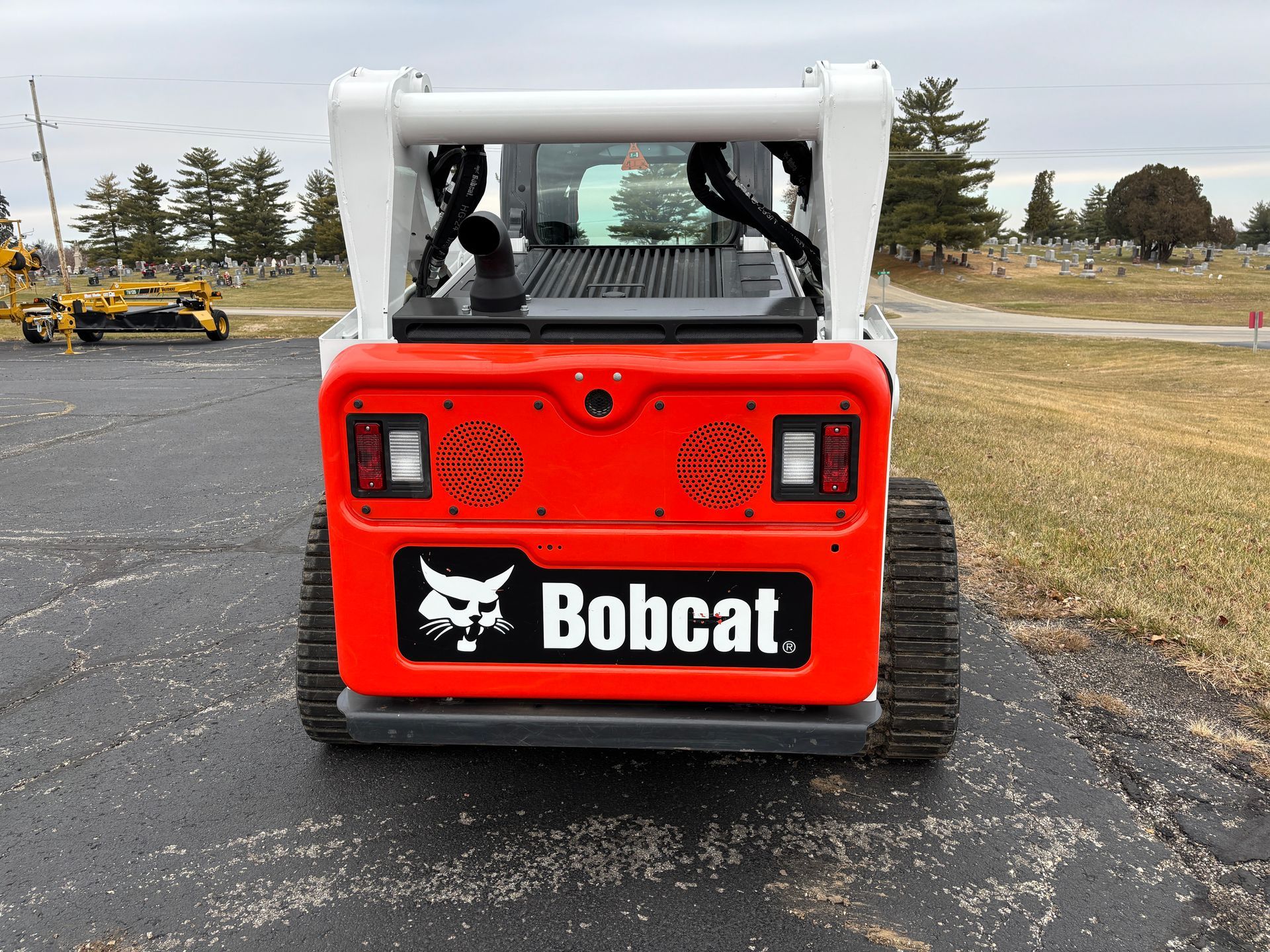 White and black Bobcat compact track loader with a bucket, outdoors on pavement, back shot.