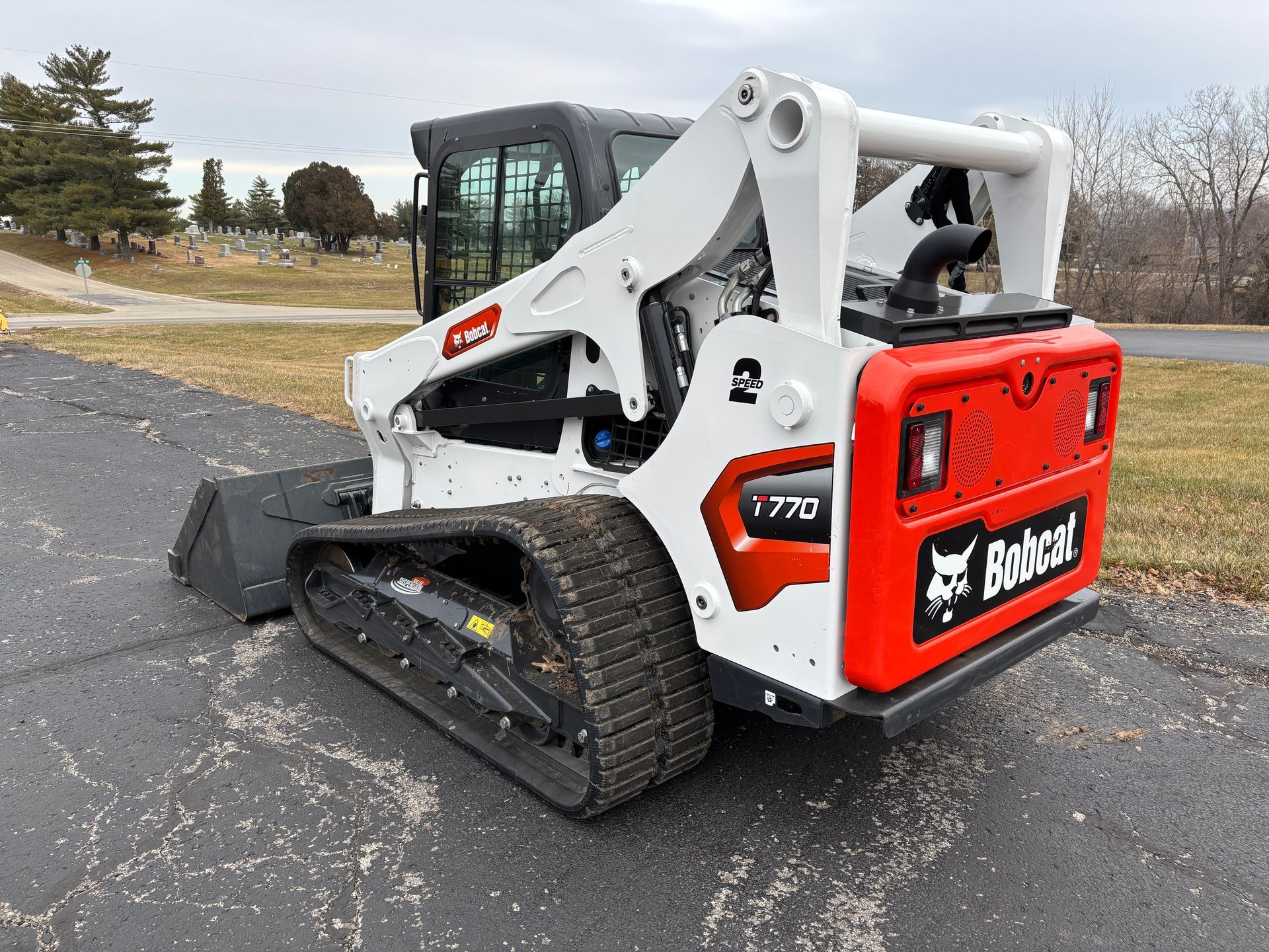 White and black Bobcat compact track loader with a bucket, outdoors on pavement, back angled shot.
