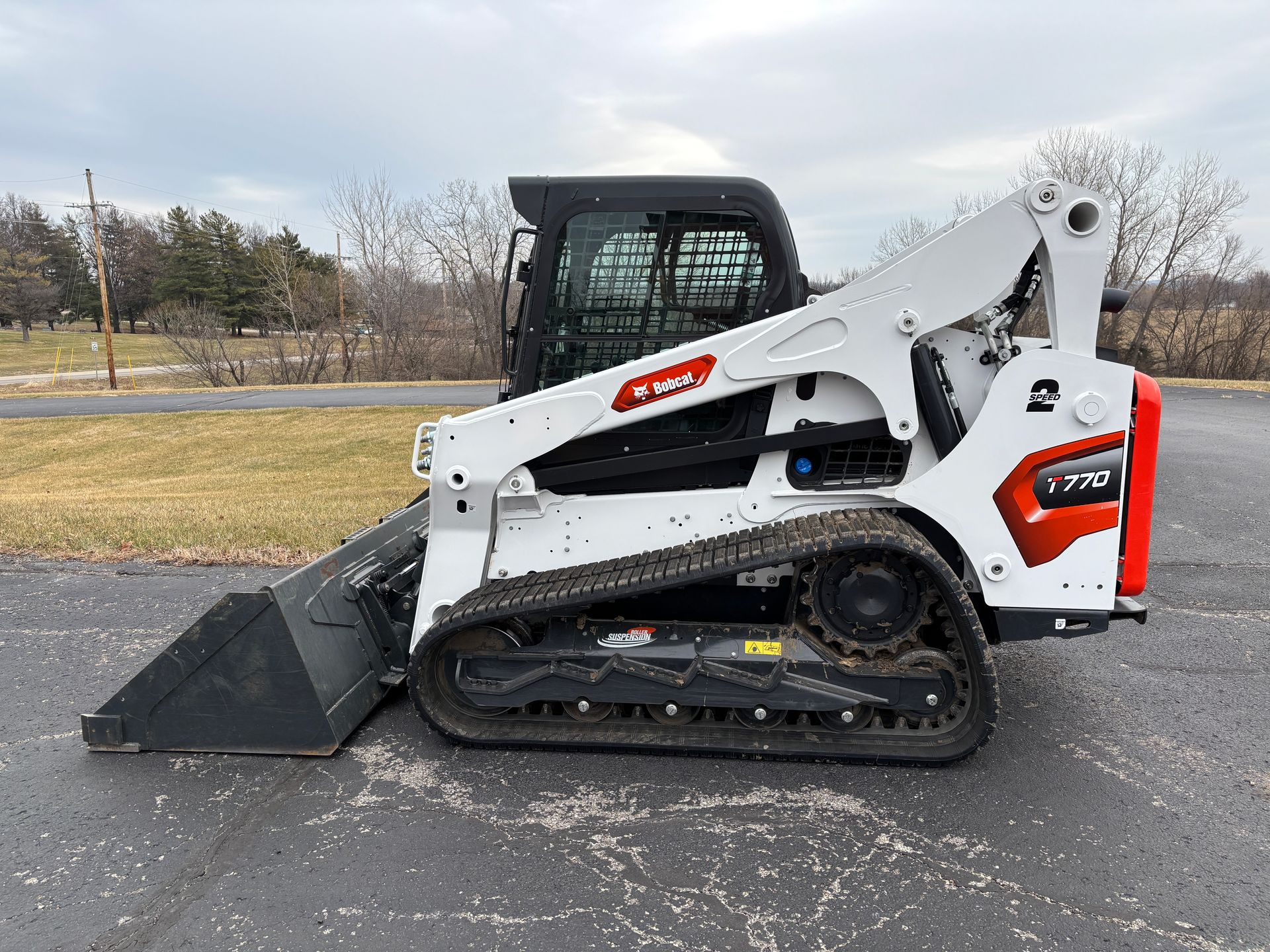 White and black Bobcat compact track loader with a bucket, outdoors on pavement, side view shot.