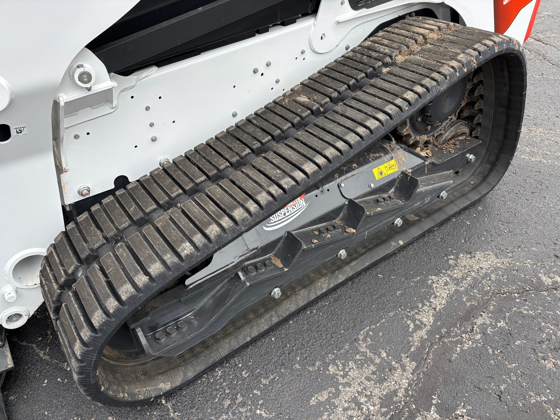White and black Bobcat compact track loader, close up of tracks, outdoors on pavement, 